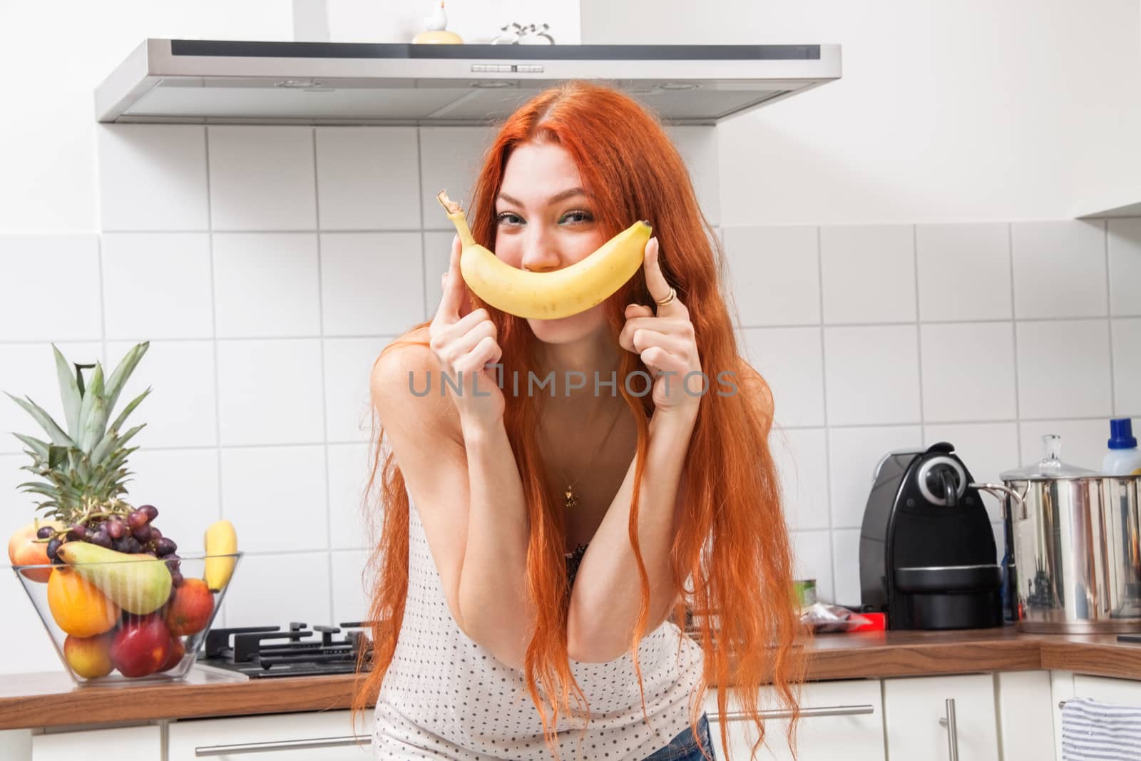 Happy Pretty Young Woman Holding a Banana Fruit, Dancing Alone at the Kitchen Inside the Home.