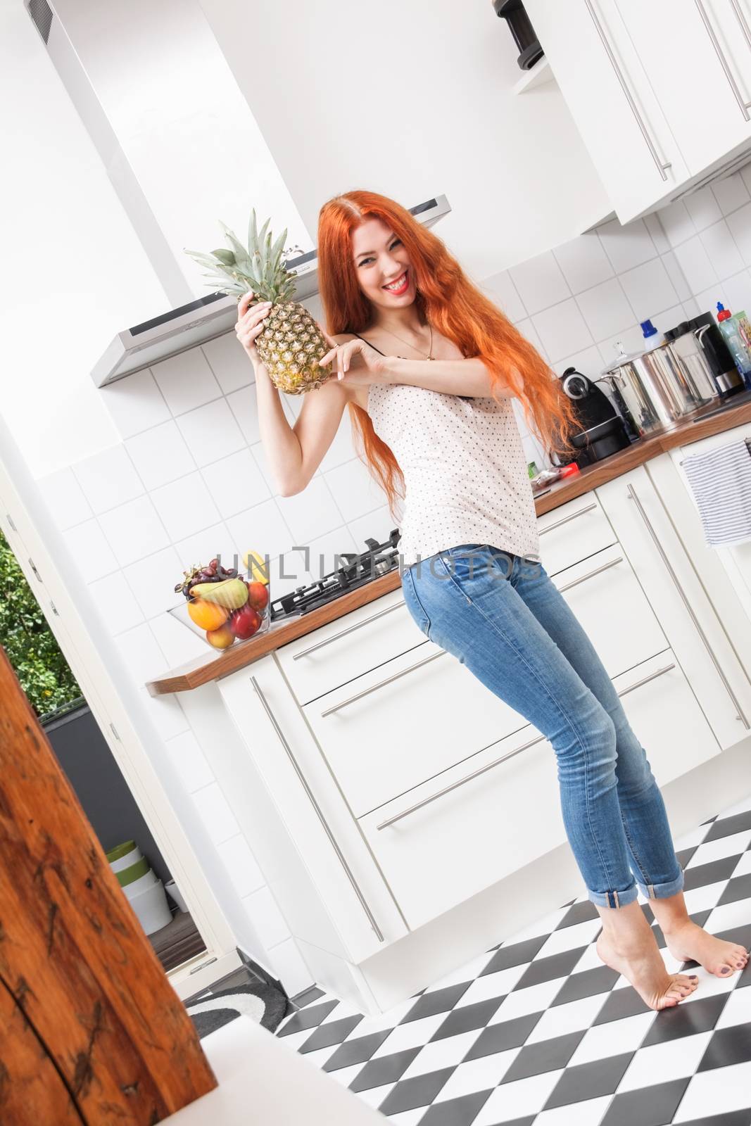 Happy Young Woman Using a Pineapple Fruit as Microphone While Singing Out Loud In the Kitchen.