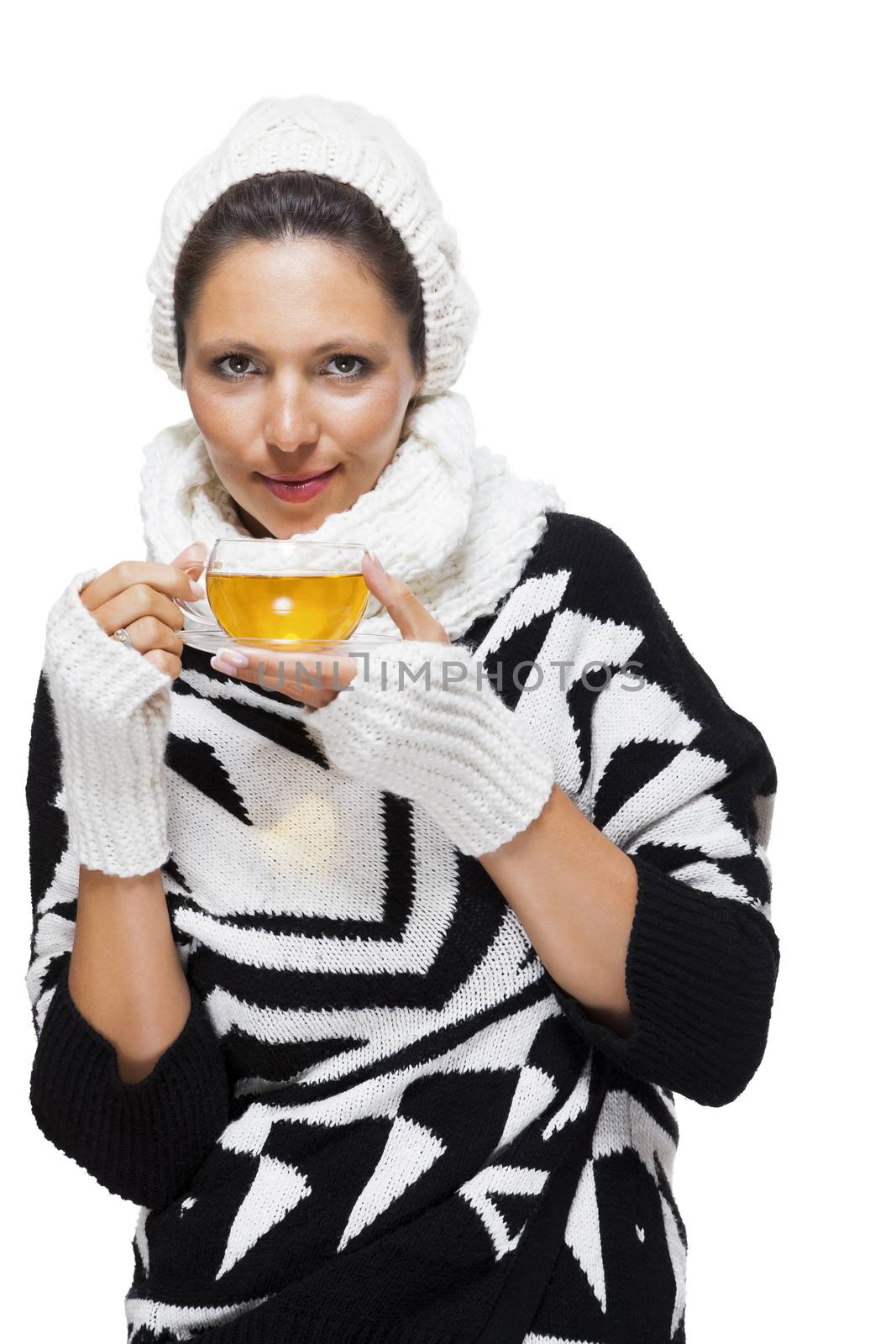 Elegant woman in a stylish black and white winter outfit with matching white mitts, scarf and knitted hat drinking a cup of hot tea, isolated on white
