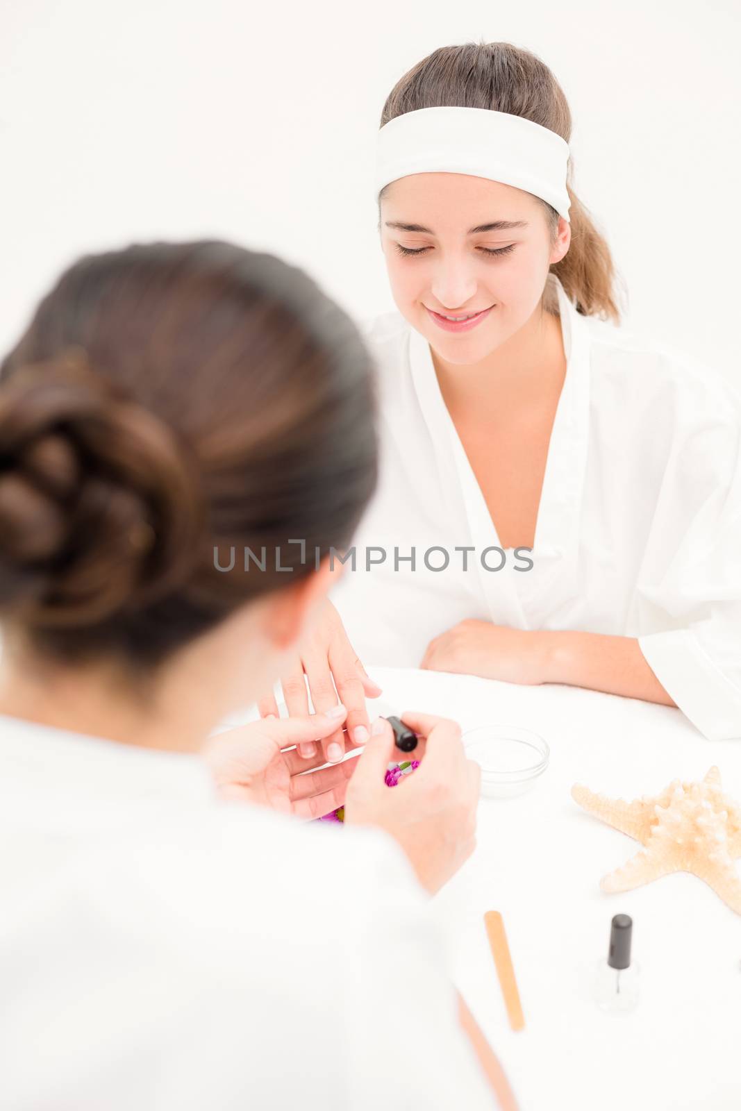 Close up of beautician applying nail varnish to female client nails at spa beauty salon