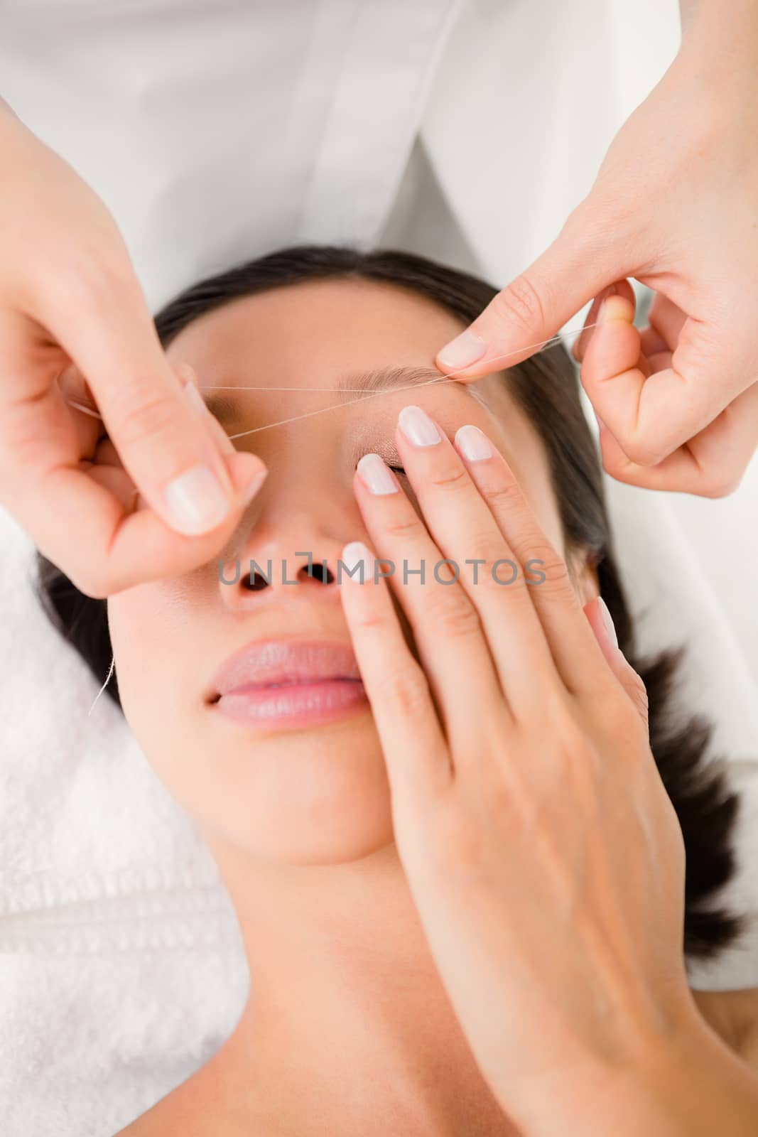 Close up view of hands threading beautiful womans eyebrow