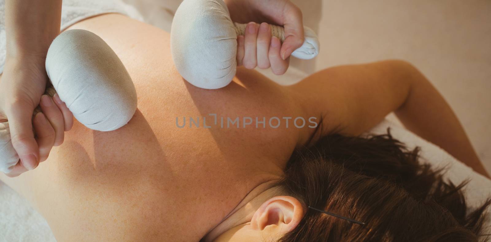 Young woman getting herbal compress massage in therapy room