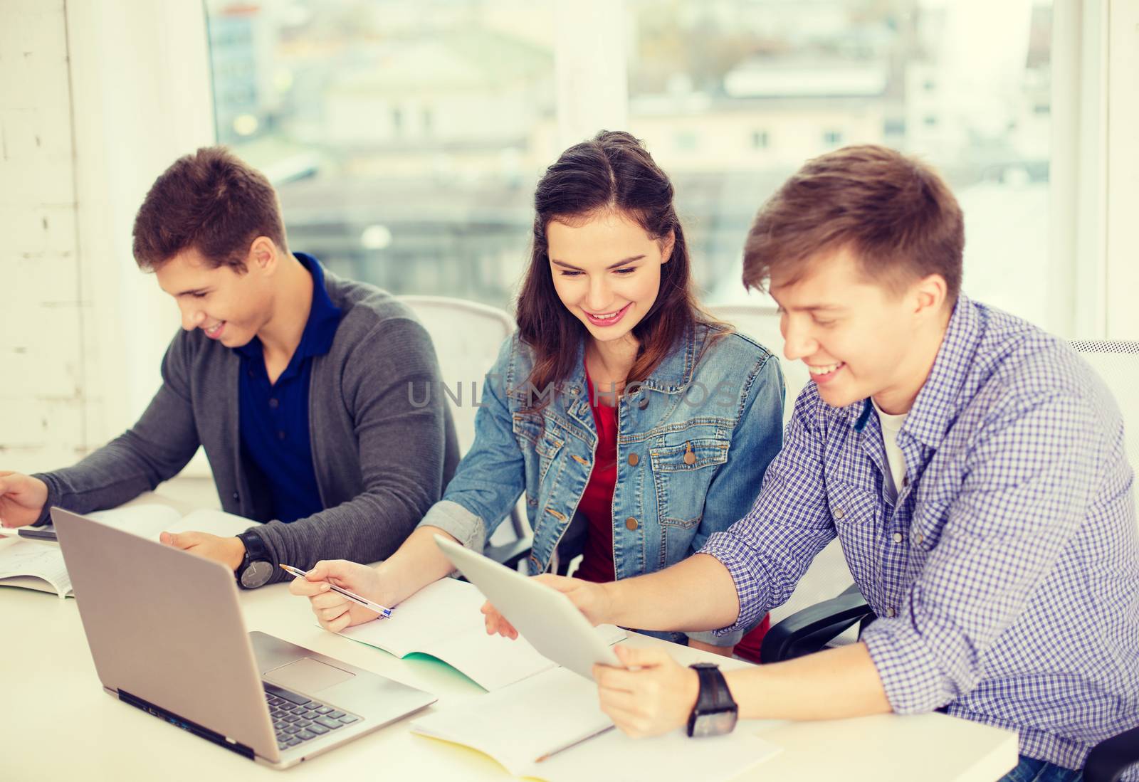 education, technology, school and internet concept - three smiling students with laptop, tablet pc and notebooks at school