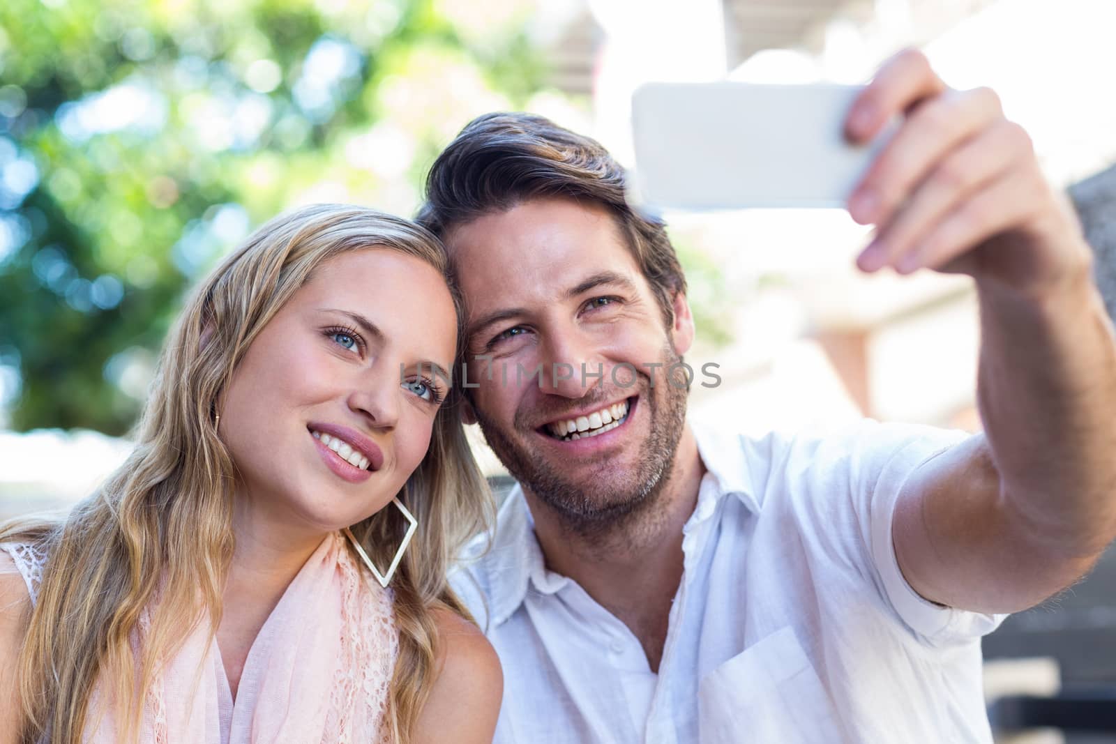 Smiling couple sitting and taking selfies by Wavebreakmedia
