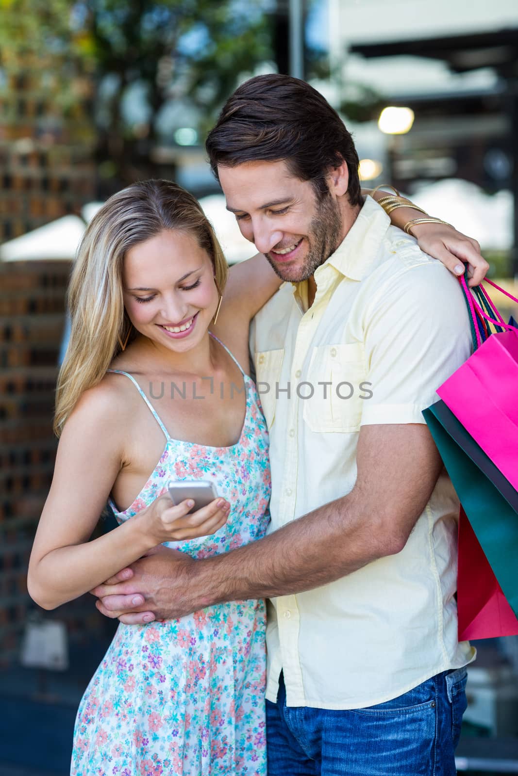 Smiling couple embracing and looking at smartphone at shopping mall