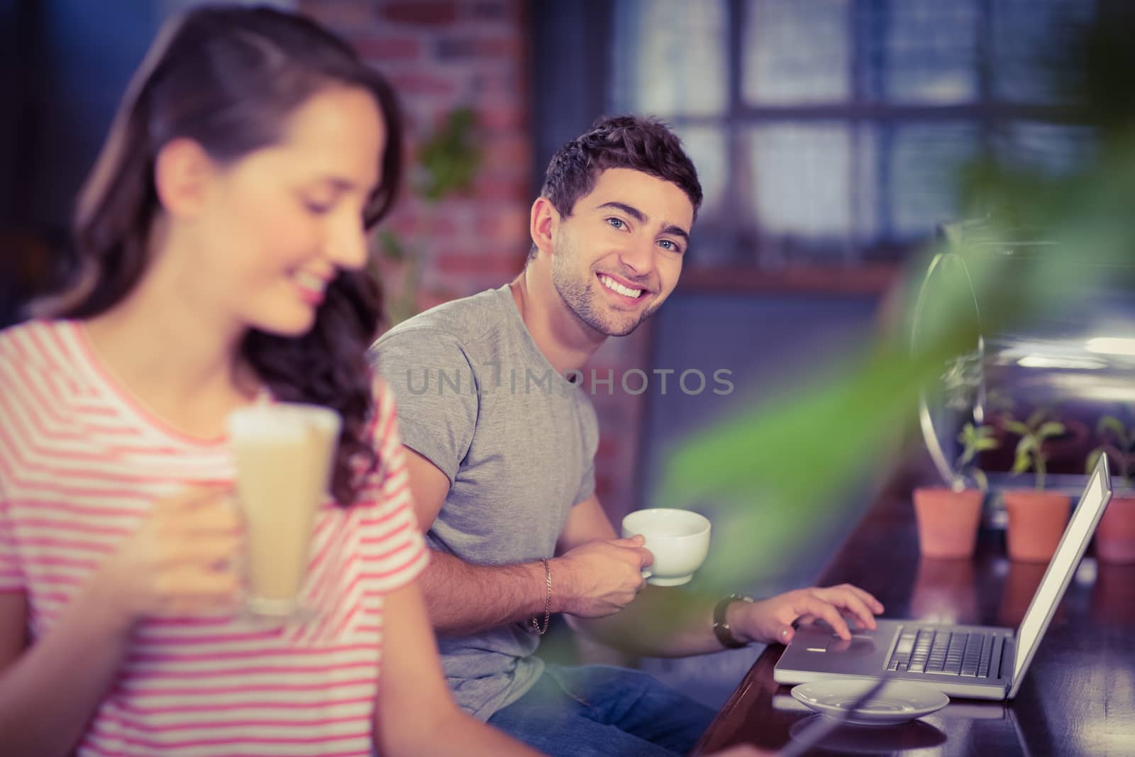 Portrait of smiling young man sitting at bar and using laptop at coffee shop