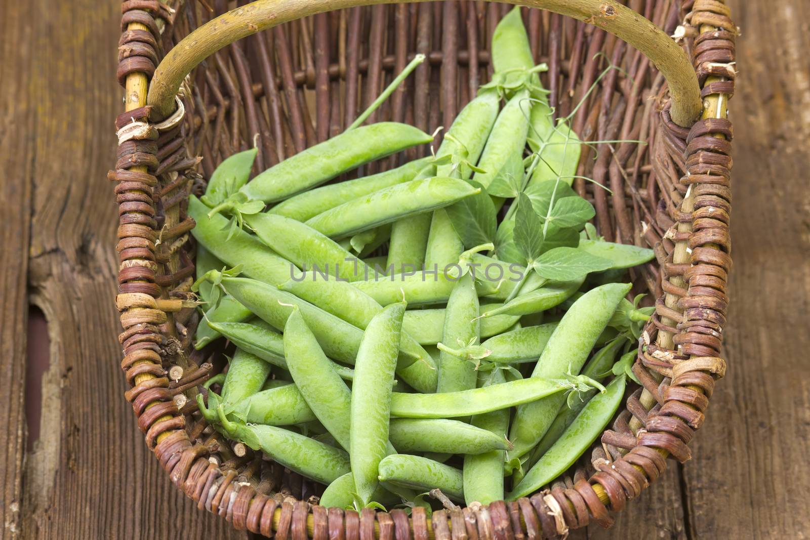wicker basket full of green peas on wooden background by miradrozdowski