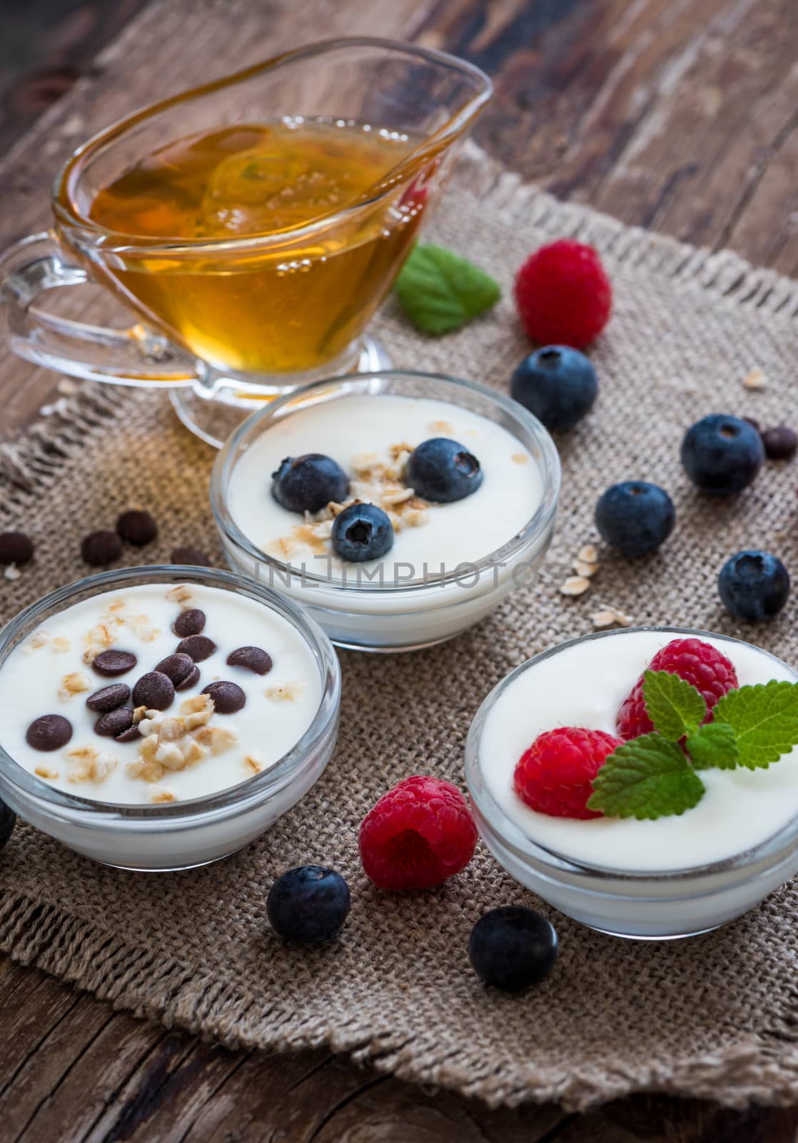 Three Little Bowls Full of Healthy Yogurt with Fruit or Chocolate and Honey on Wooden Rustic Table