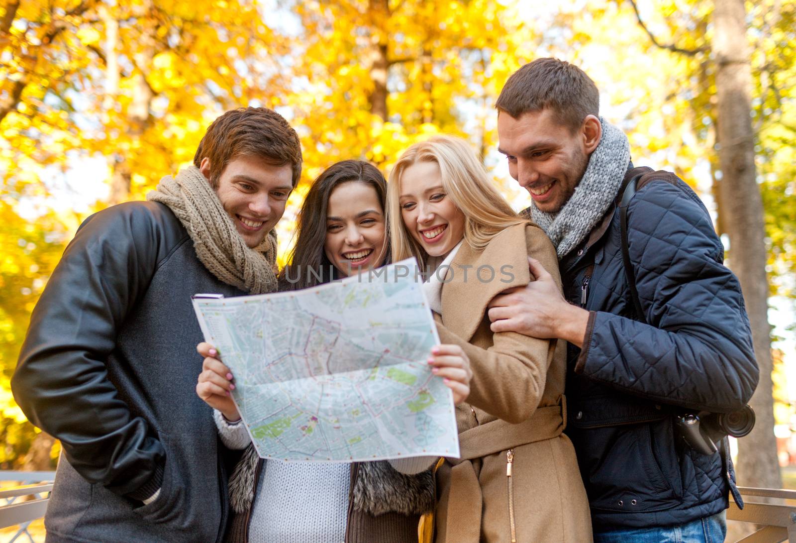 travel, vacation, people, tourism and friendship concept - group of smiling friends looking to map in city park