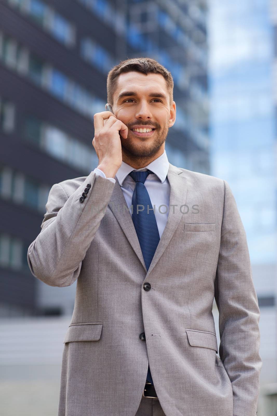 business, technology and people concept - smiling businessman with smartphone talking over office building