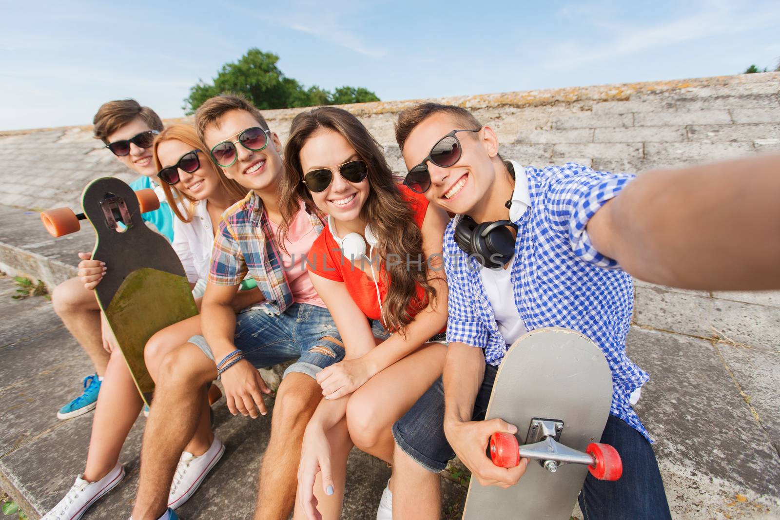 friendship, leisure, summer, technology and people concept - group of smiling friends with skateboard making selfie outdoors