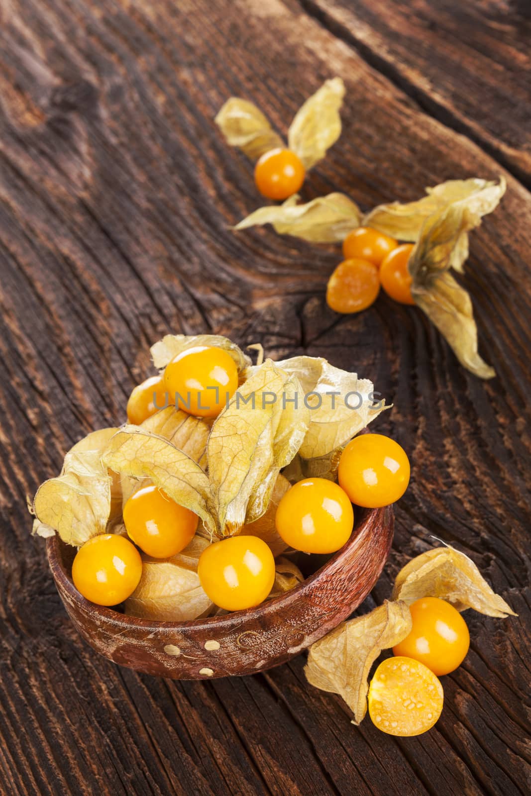 Physalis, groundcherries in bowl on brown textured aged background. Tropical healthy fruit eating.
