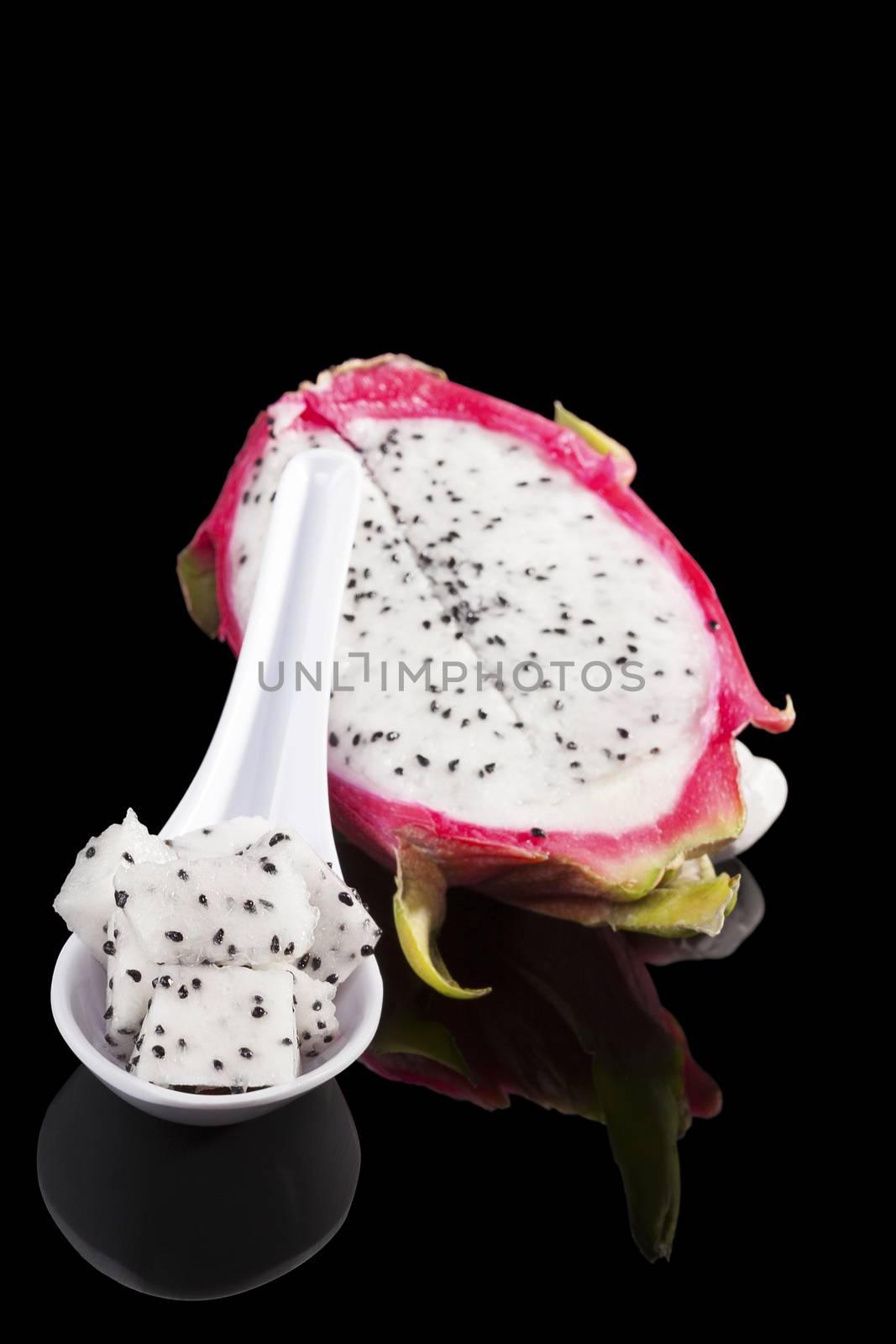 Dragon fruit pieces on spoon isolated on black background. Tropical fruit salad.