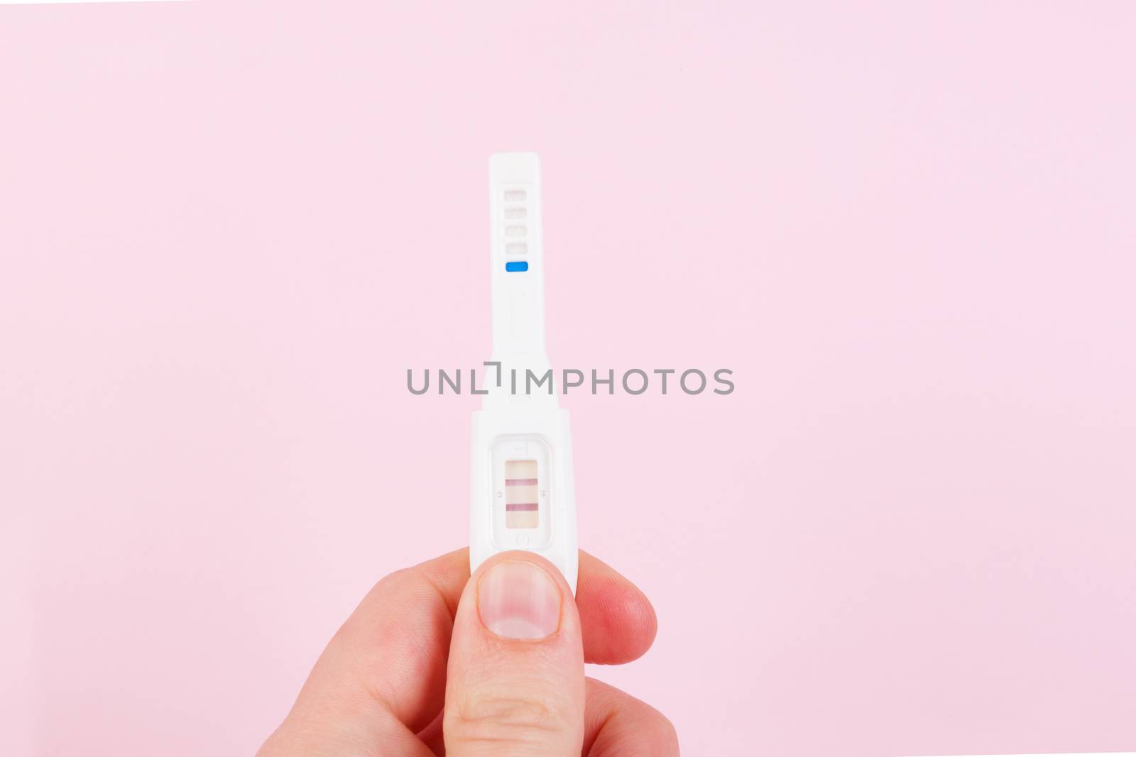 Male hand holding positive pregnancy test isolated on pink background. Happy father.