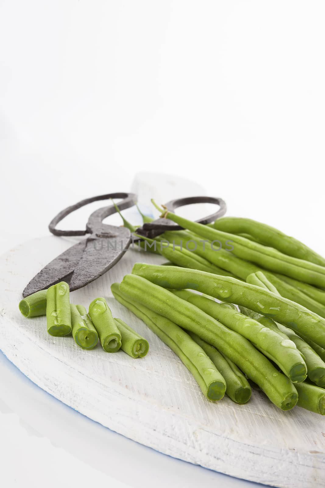 Green beans with water drops on wooden chopping board with vintage scissors isolated on white background. Healthy eating. 