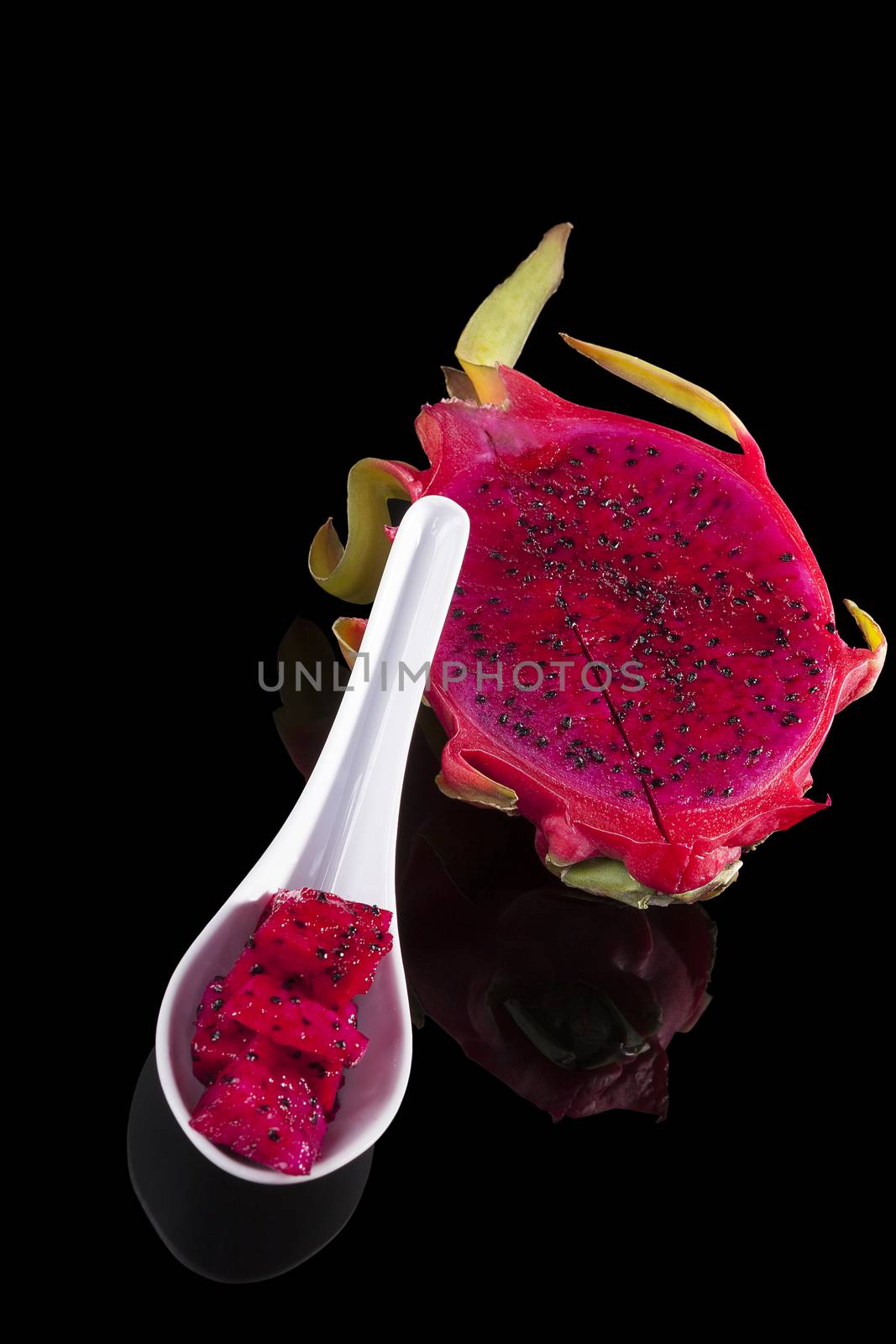Dragon fruit pieces on spoon isolated on black background. Tropical fruit salad.