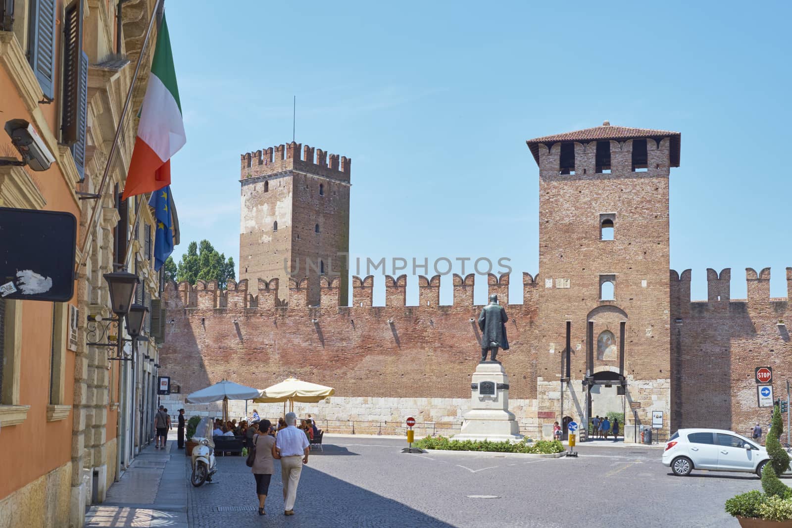VERONA, ITALY - JULY 11: Pedestrians in front of Castelvecchio castle, with Italian flag in the foreground. July 11, 2015 in Verona.
