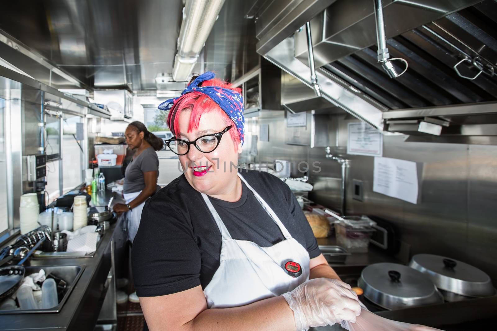 Pink haired chef puts on work gloves aboard busy food truck