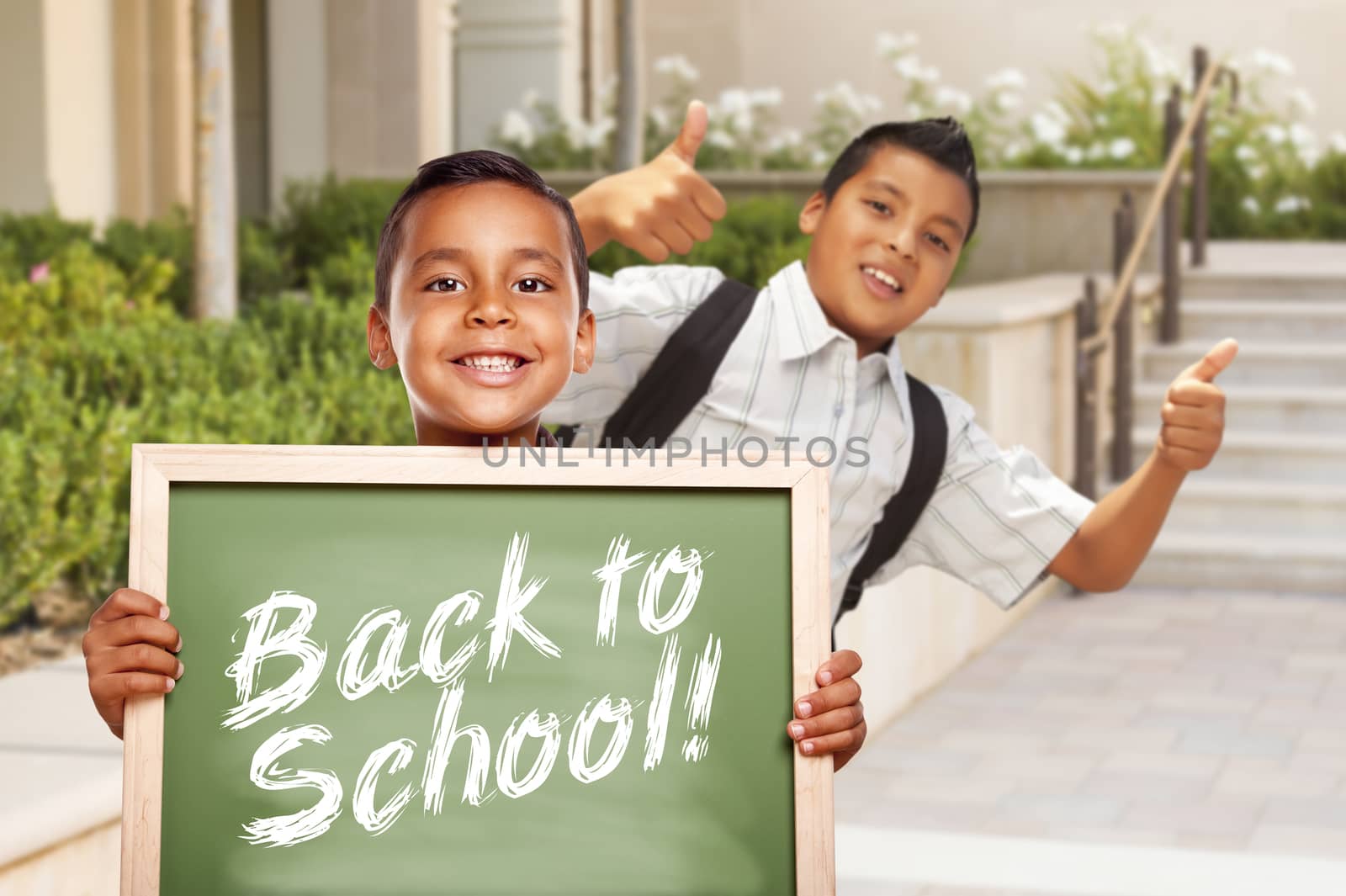 Happy Hispanic Boys Giving Thumbs Up Holding Back to School Chalk Board Outside on School Campus.