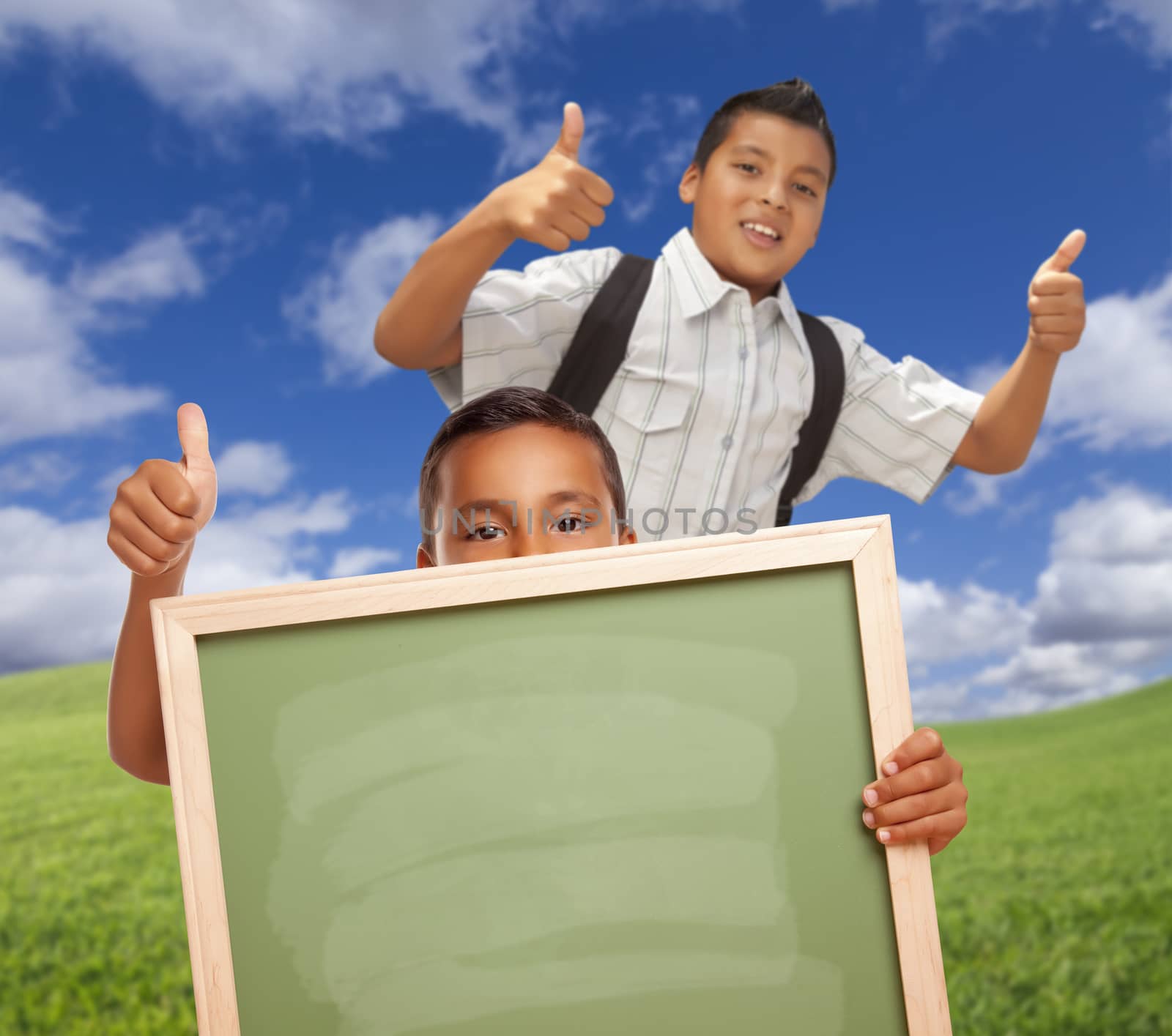Hispanic Students with Thumbs Up in Grass Field Holding Blank Chalk Board. by Feverpitched
