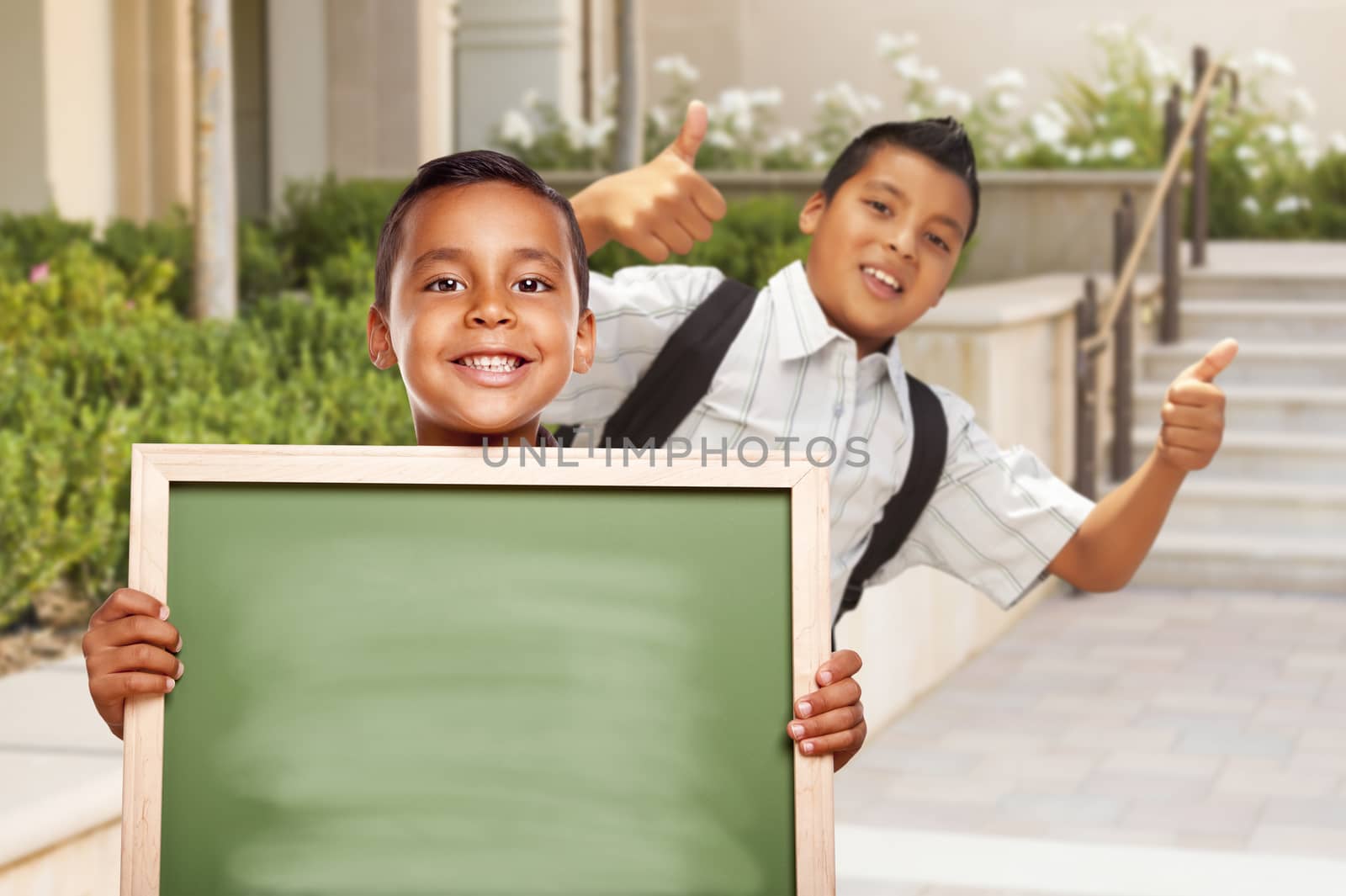 Happy Hispanic Boys with Thumbs Up Holding Blank Chalk Board Outside on School Campus.