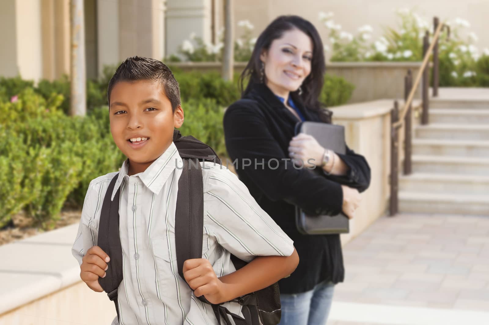 Happy Hispanic Boy with Backpack on School Campus and Teacher Behind.