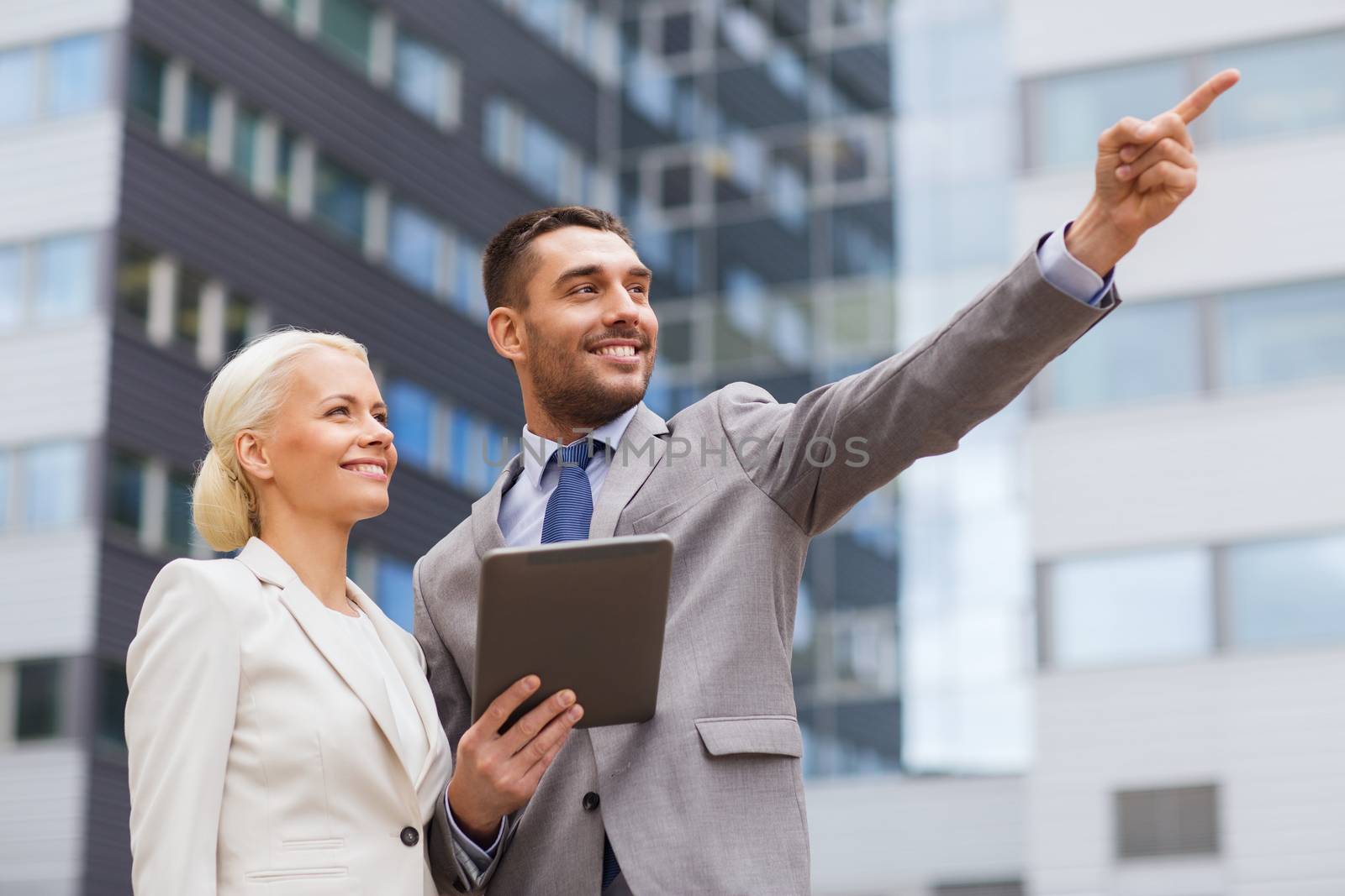 business, partnership, technology and people concept - smiling businessman and businesswoman with tablet pc computer over office building