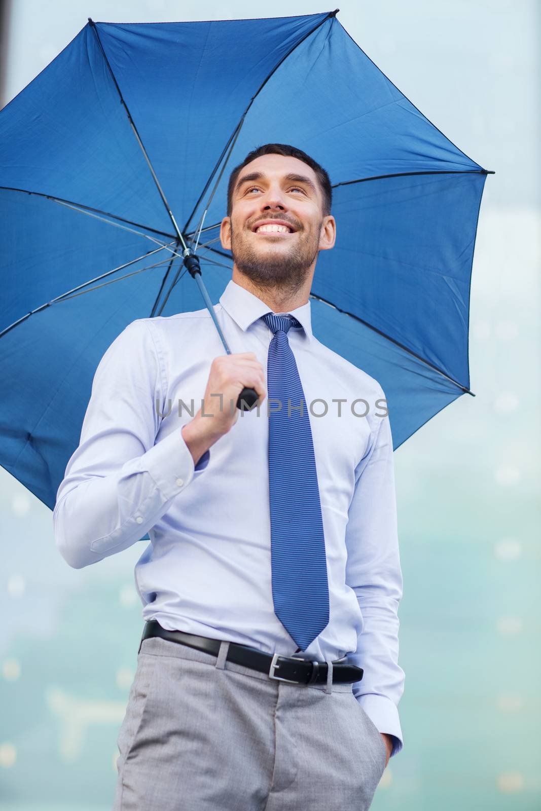 young smiling businessman with umbrella outdoors by dolgachov