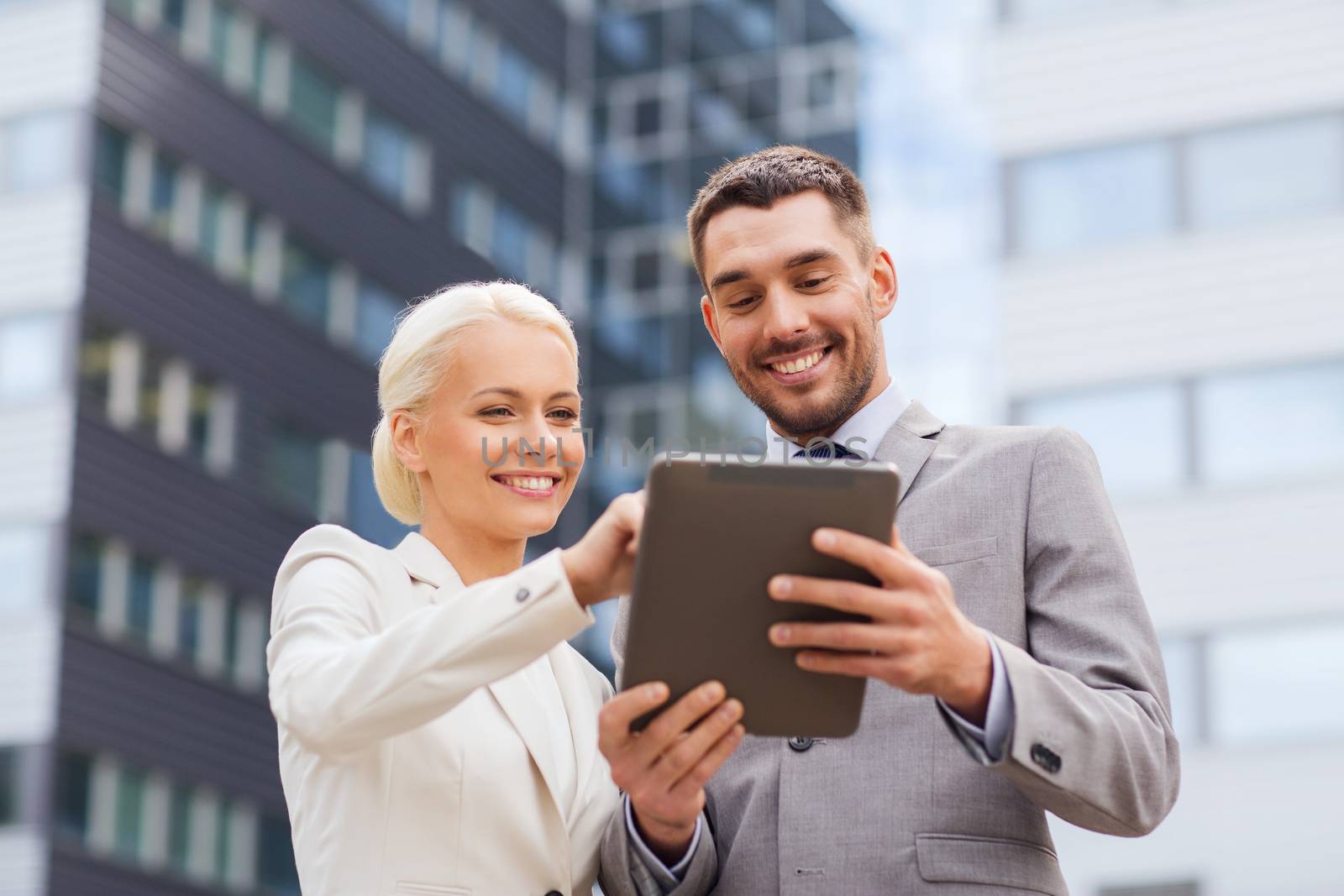 business, partnership, technology and people concept - smiling businessman and businesswoman with tablet pc computer over office building