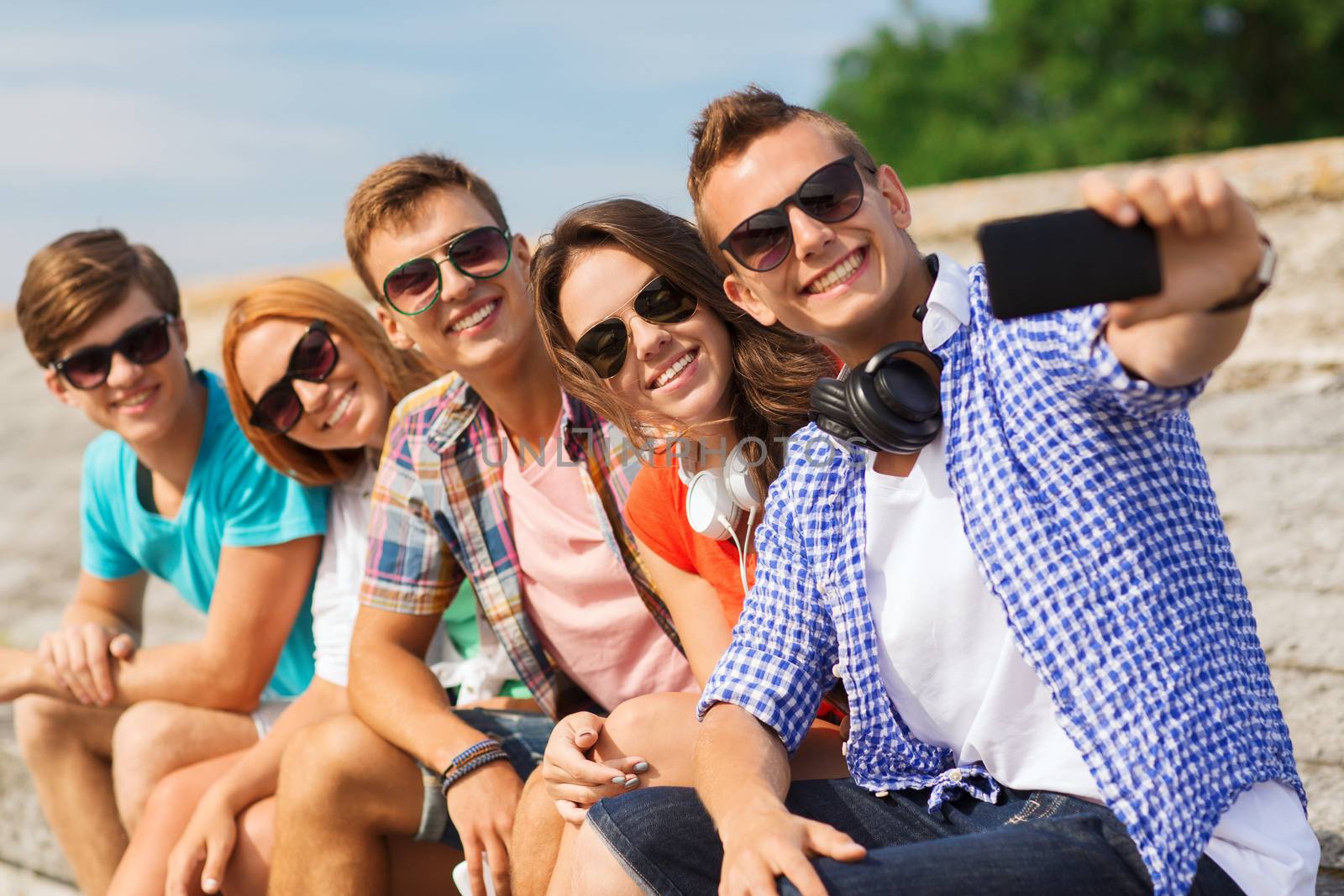 group of smiling friends with smartphone outdoors by dolgachov