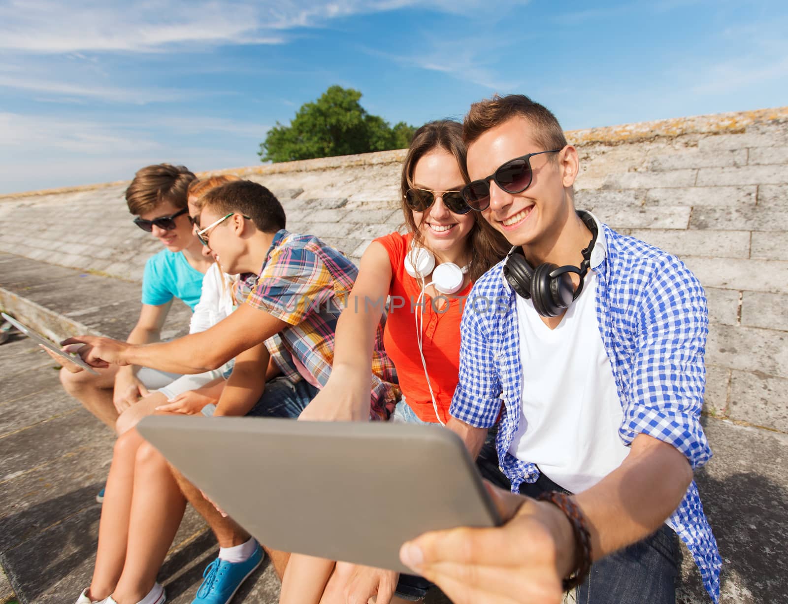 friendship, leisure, summer and people concept - group of smiling friends with tablet pc computers sitting outdoors