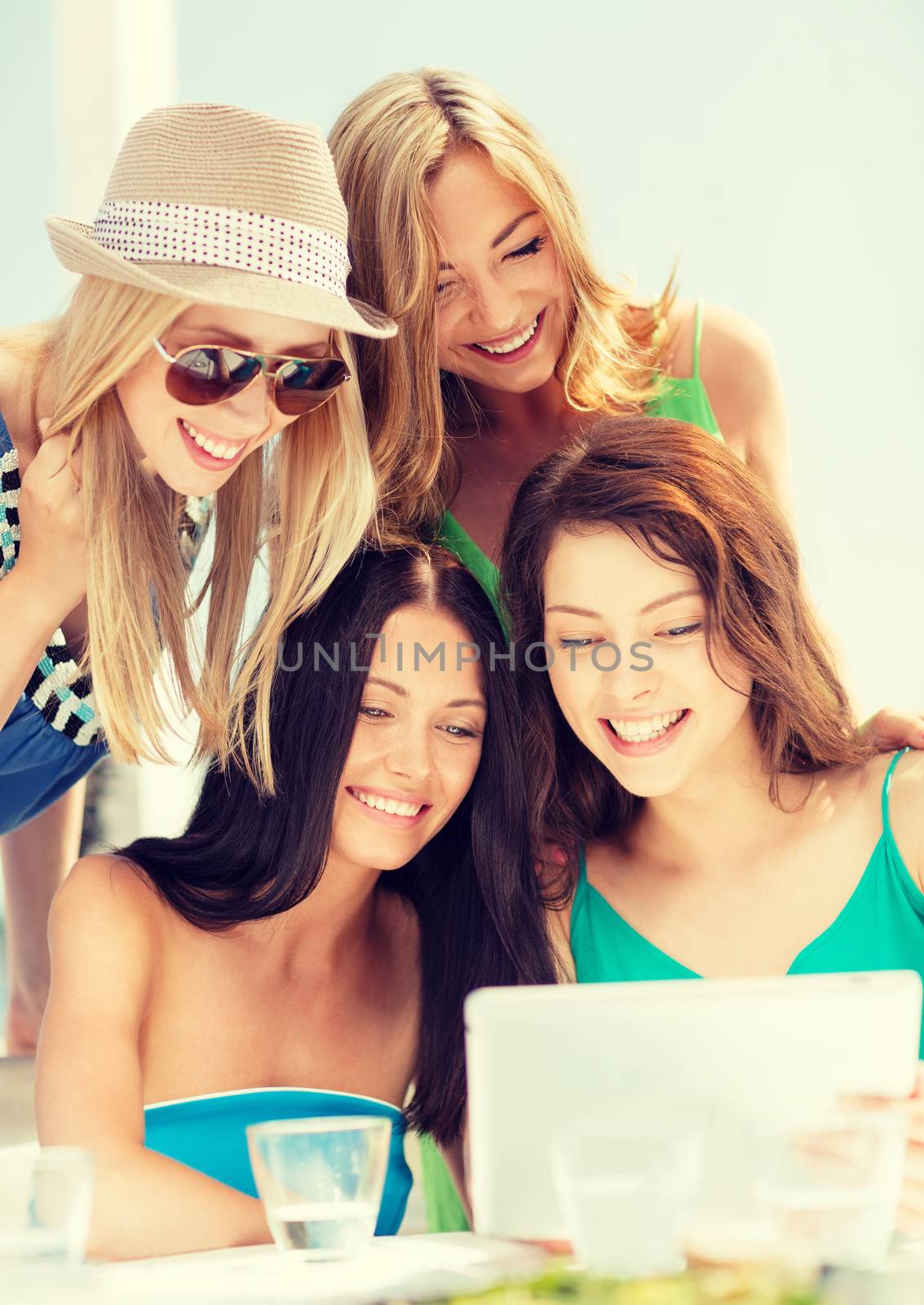 smiling girls looking at tablet pc in cafe by dolgachov