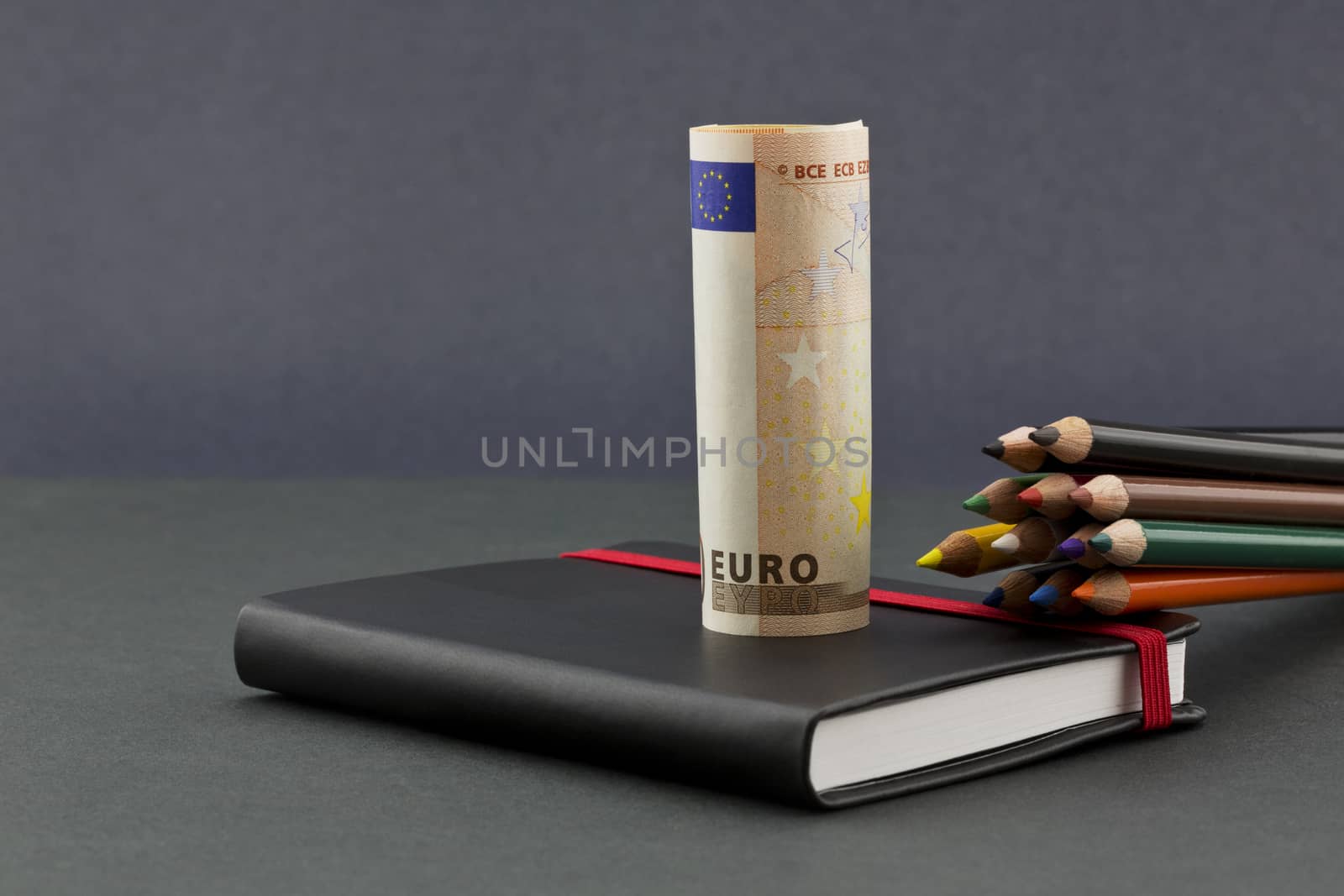 Business opportunities and challenges for the euro reflected in multiple colors of pencils, euro currency, and black journal with red elastic on dark background.  Copy space on horizontal image.  