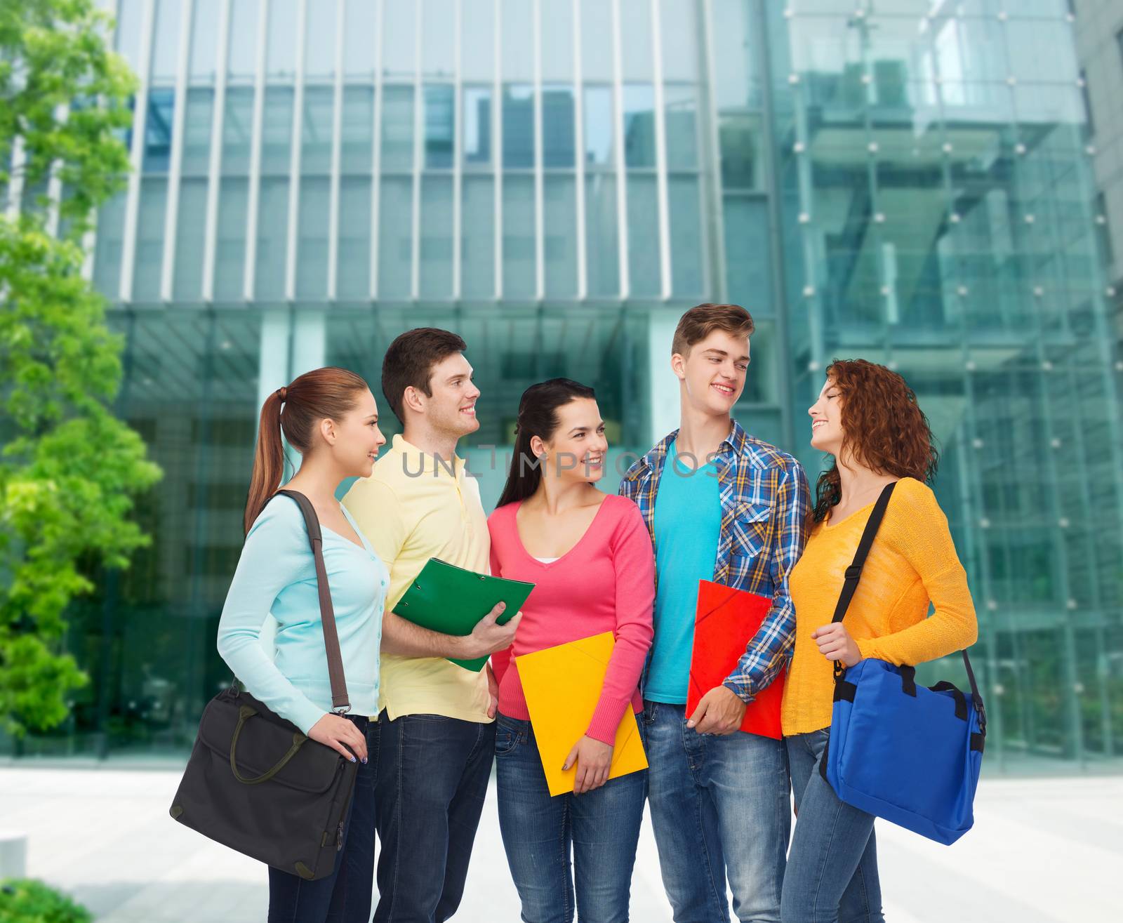 friendship, business, education and people concept - group of smiling teenagers with folders and school bags over campus background