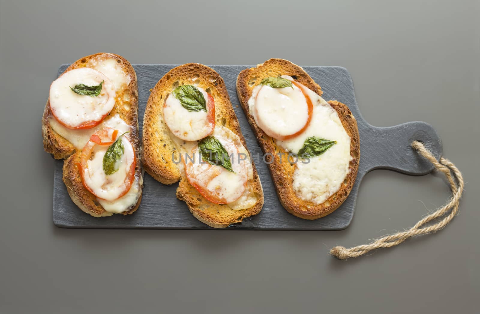 Basil tomato and cheese bruschetta over a slate rock board by noimagination