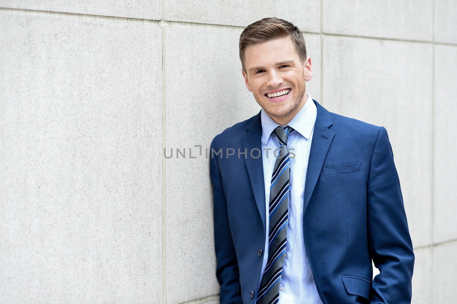 Image of a happy businessman leaning against a wall