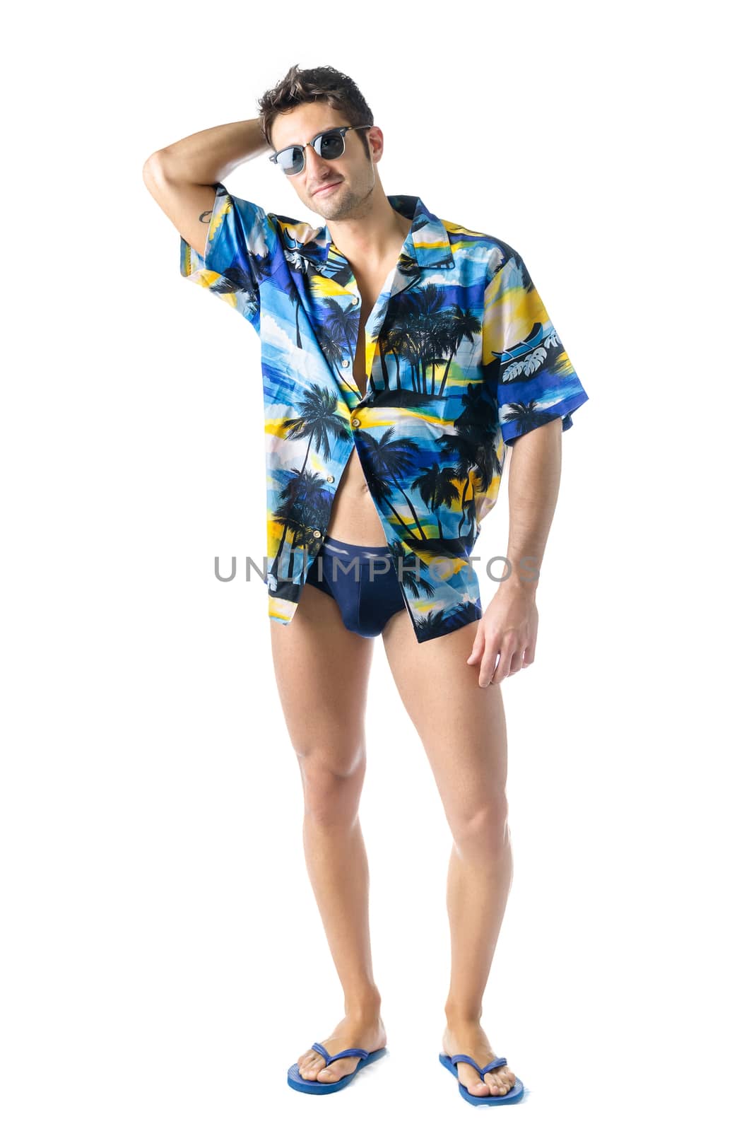 Attractive, muscular young man smiling, wearing open hawaian style shirt, swimming suit and sunglasses. Full figure shot