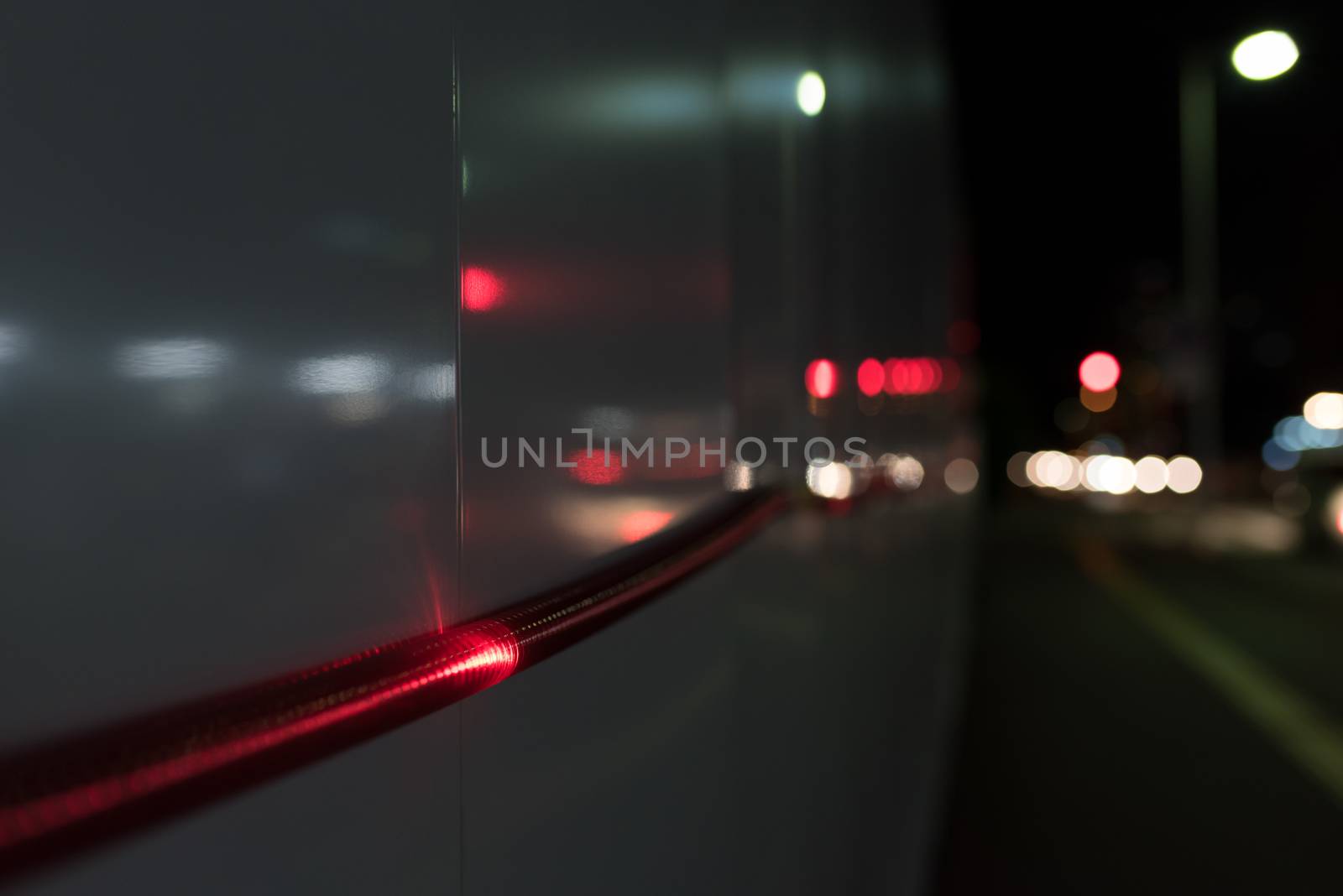 A close up shot of a red rope light going along a wall outside of a construction area at night with cars' tail lights blurred in the dark background.
