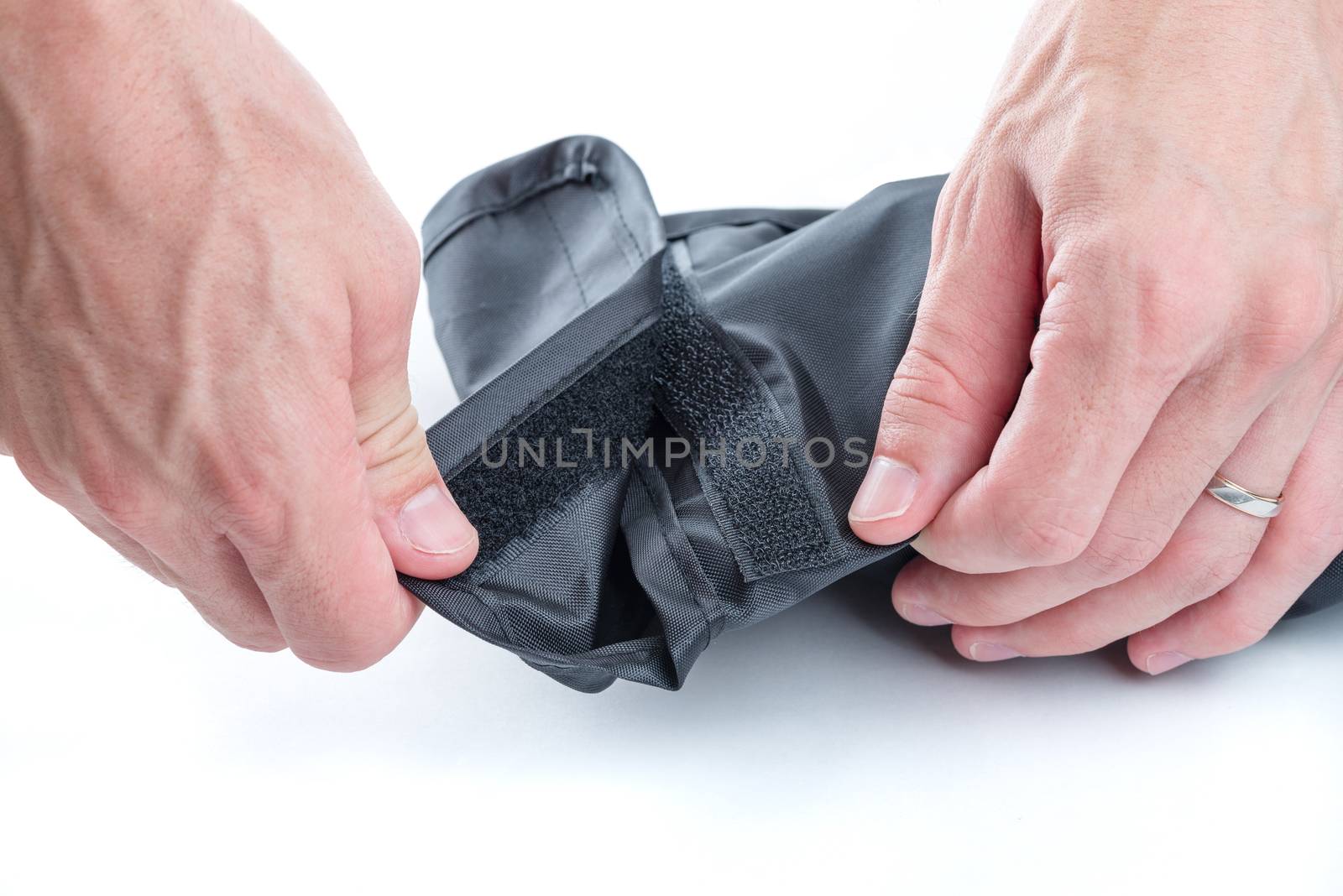 A close up shot of men's hands opening a black case closed with a velcro fastener on a white background.