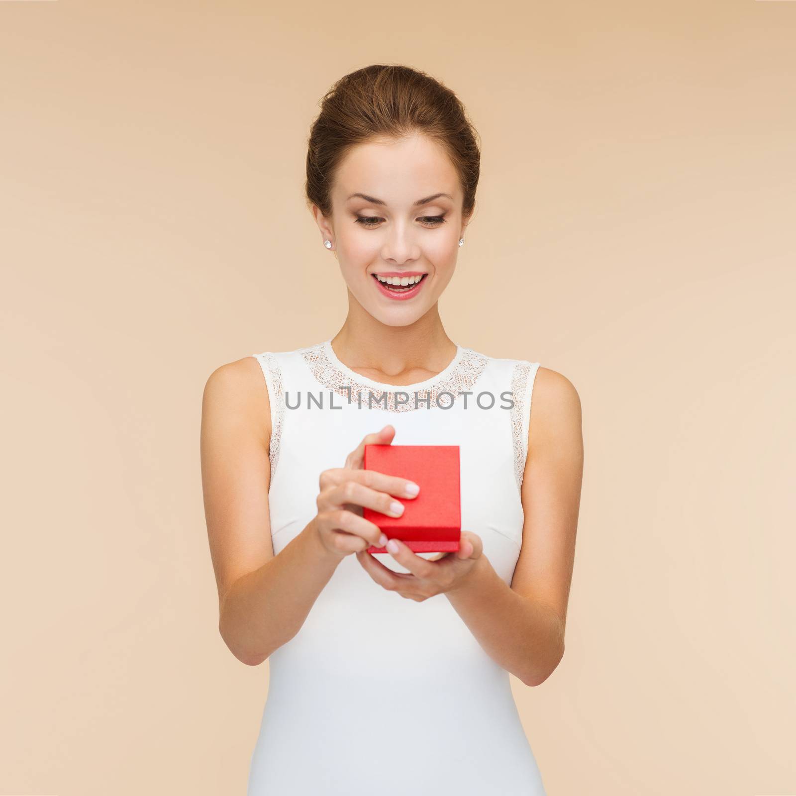 holidays, presents, wedding and happiness concept - smiling woman in white dress holding red gift box over beige background