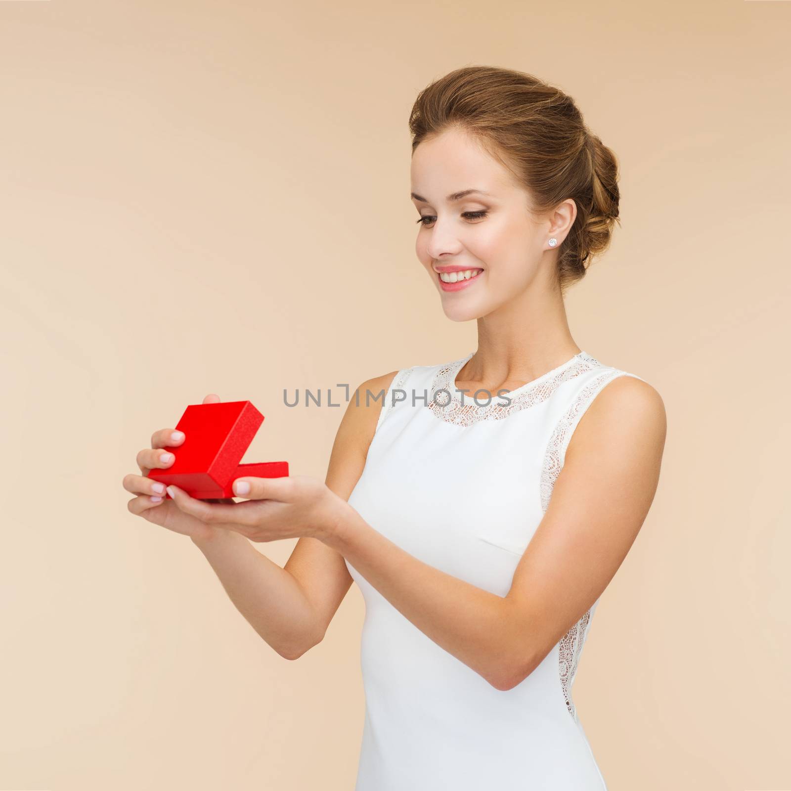 holidays, presents, wedding and happiness concept - smiling woman in white dress holding red gift box over beige background