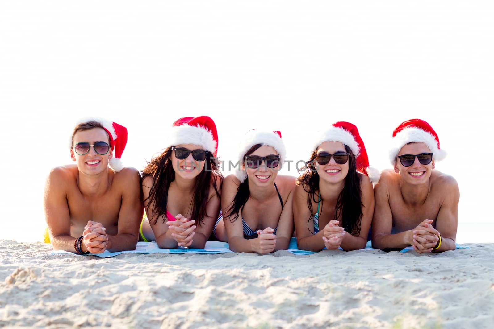 group of friends in santa helper hats on beach by dolgachov