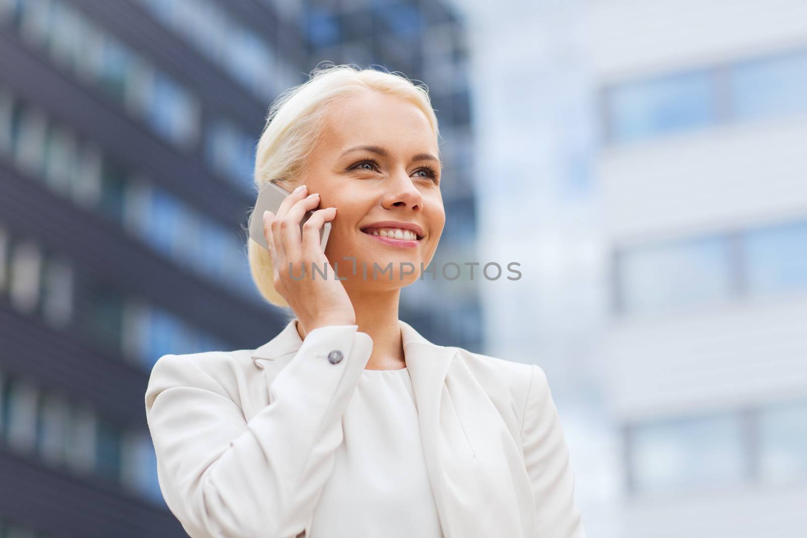 business, technology and people concept - smiling businesswoman with smartphone talking over office building