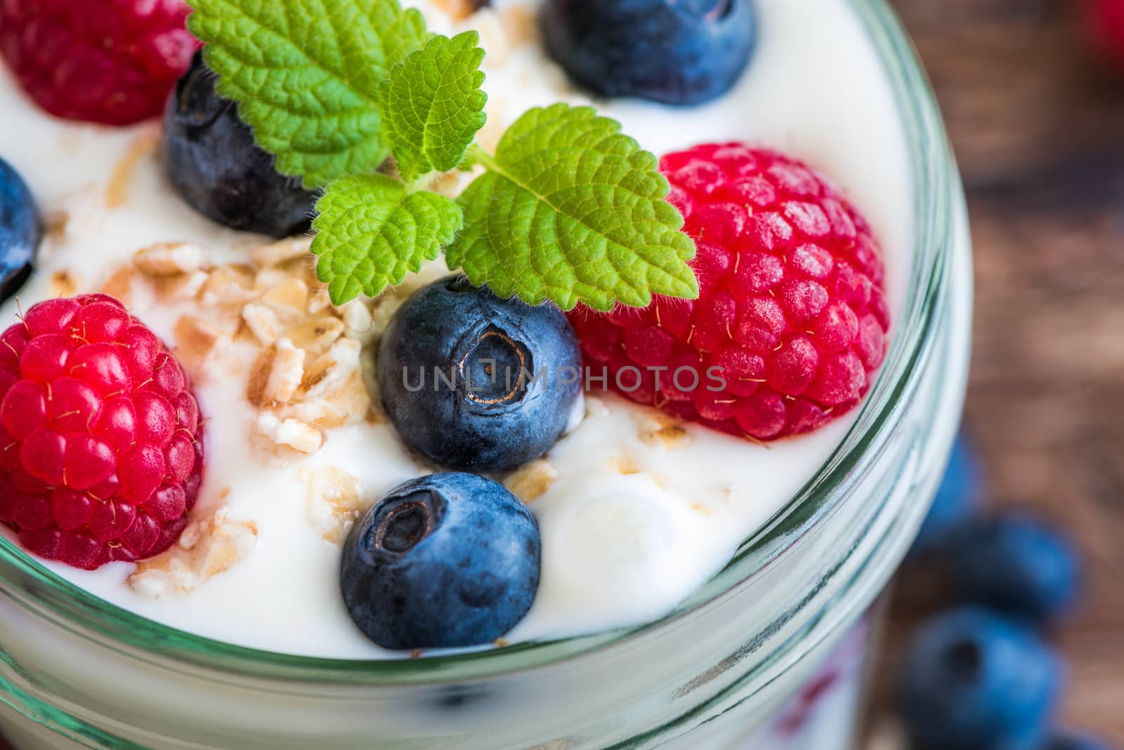 Serving of Yogurt with Whole Fresh Blueberries, Raspberries and Oatmeal on Old Rustic Wooden Table. Closeup Detail.