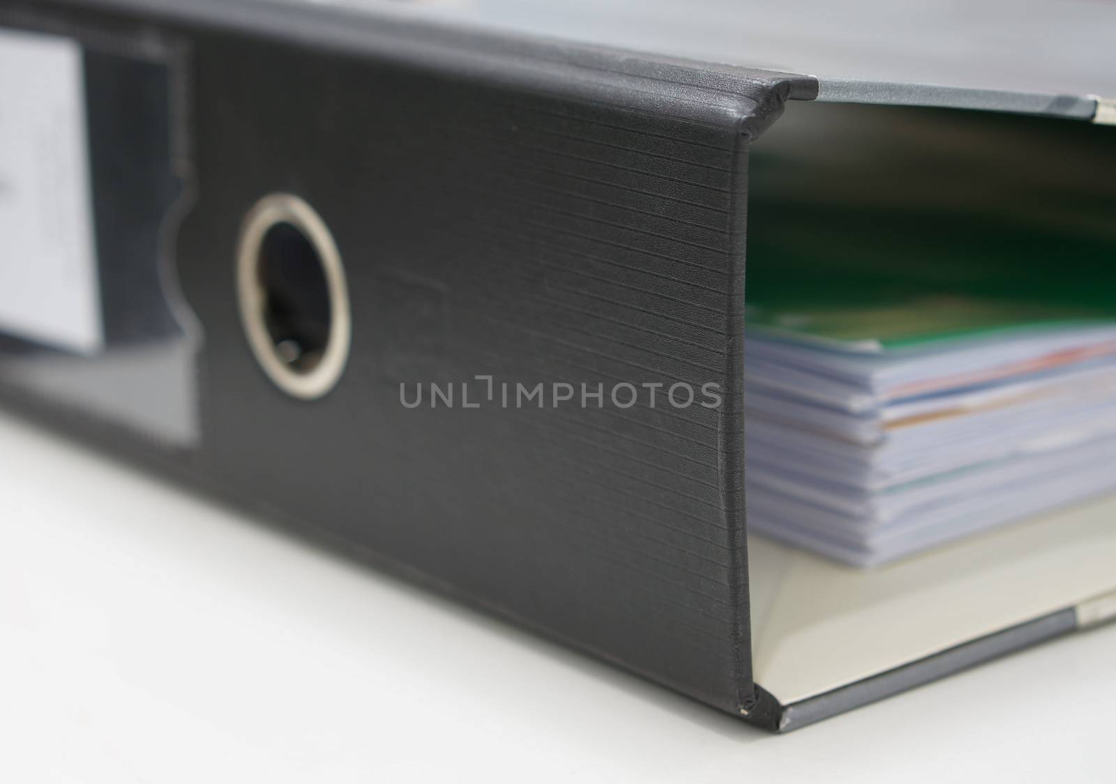 Stack of documents in black binders on desk at office.                        