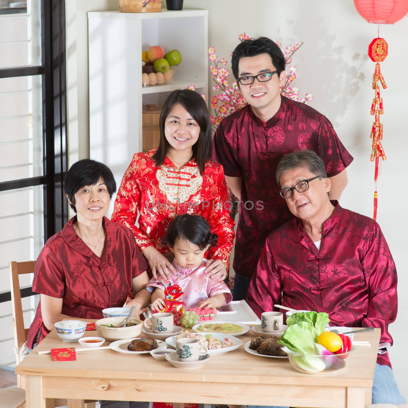 Spring seasons Chinese New Year, reunion dinner. Happy Asian Chinese multi generation family with red cheongsam taking group photo while dining at home.
