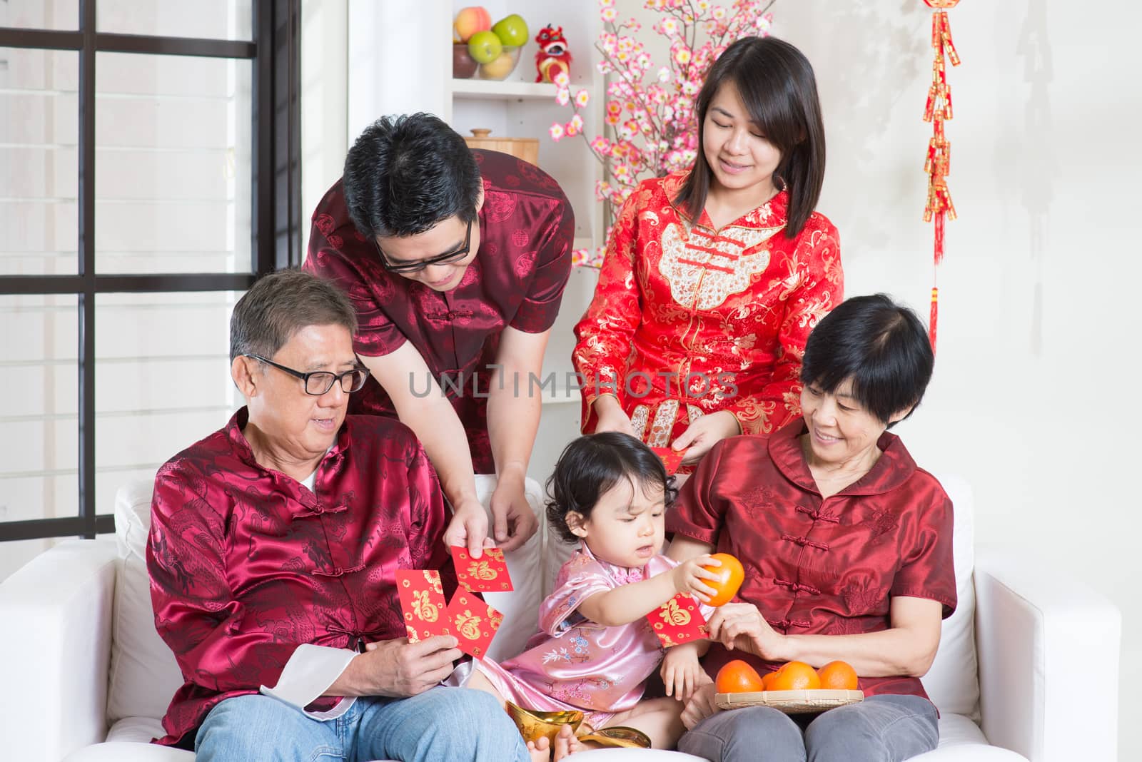 Chinese new year celebration. Happy Asian multi generations family in red cheongsam showing red packets while reunion at home.