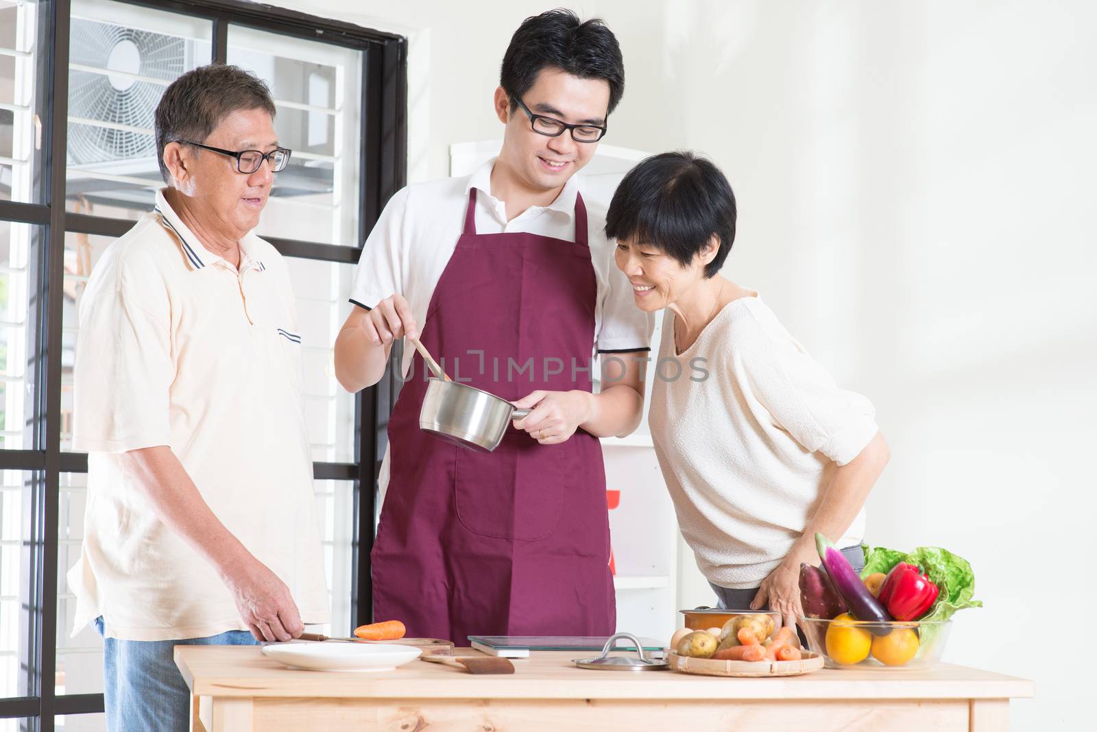 Asian adult son preparing meal for his senior parents at kitchen. Family living lifestyle at home.