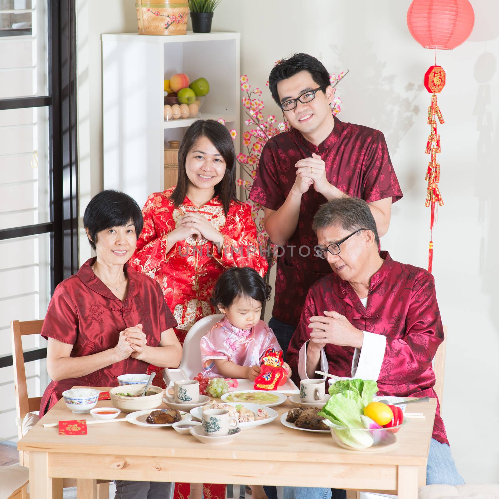 Spring seasons Chinese New Year, reunion dinner. Happy Asian Chinese multi generation family with red cheongsam greeting while dining at home.
