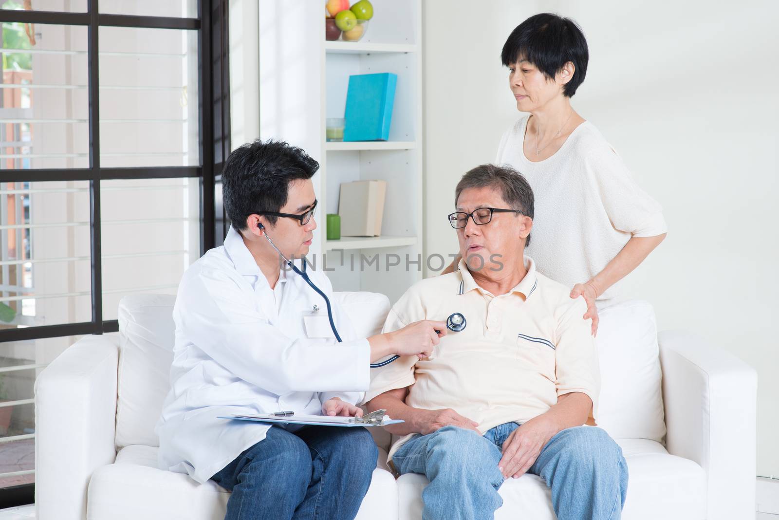 Doctor and patient. Sick Asian old man consult family doctor, sitting on sofa. Senior retiree indoors living lifestyle.